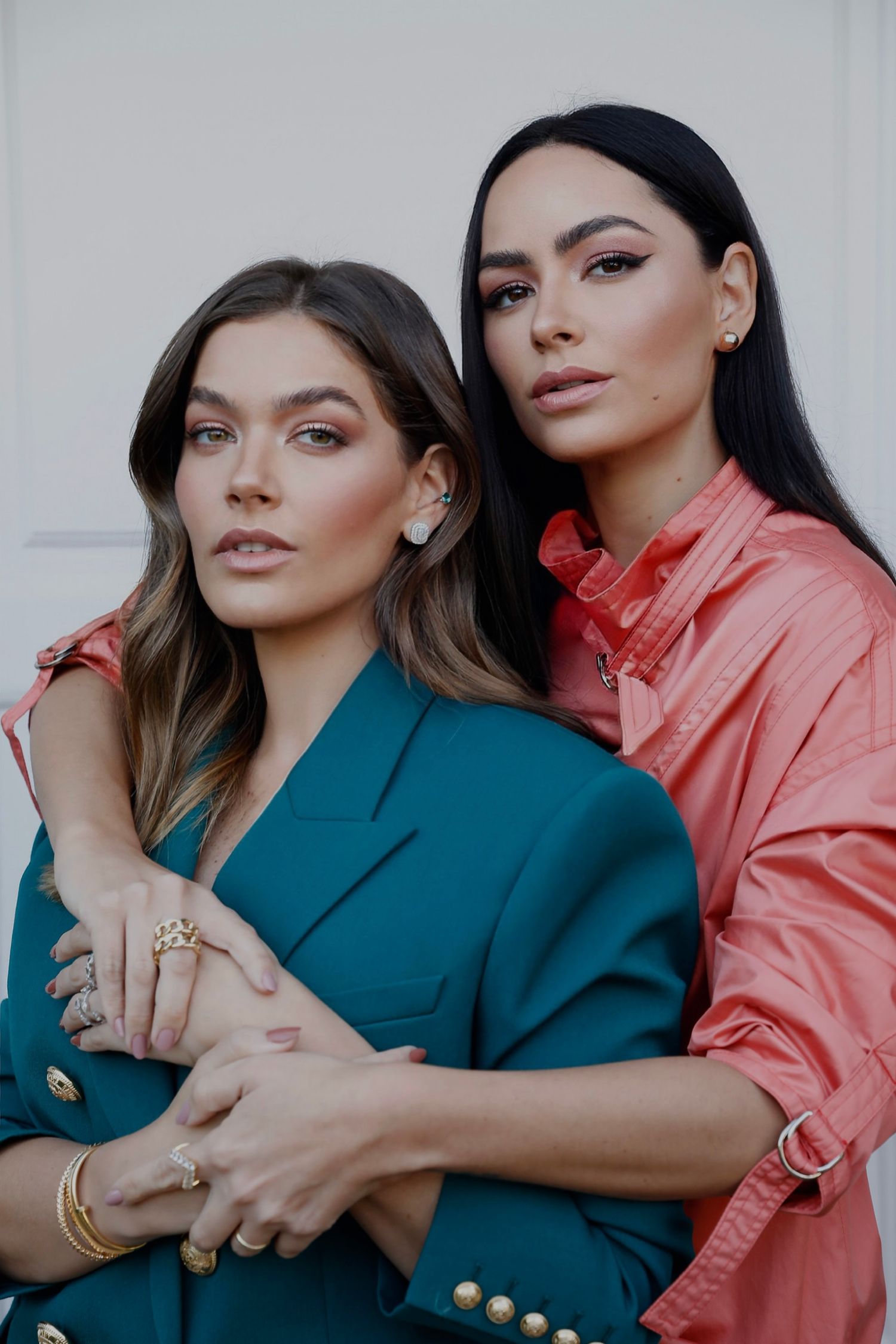 Two models posing in teal and coral business attire against white backdrop.