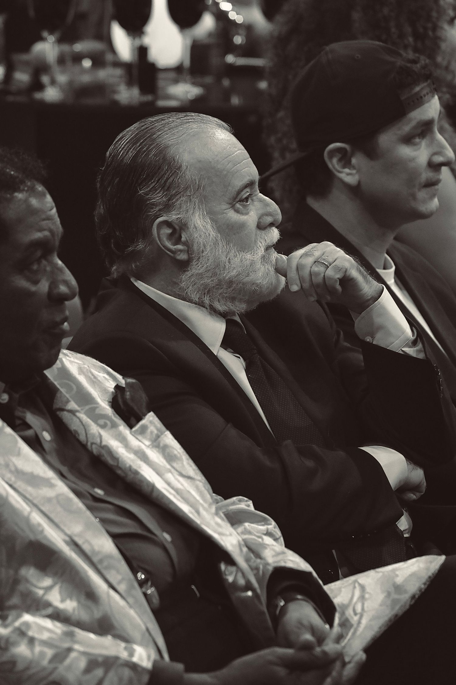 Black and white photograph of people seated at a formal event, with some in suits and others in light colored attire.