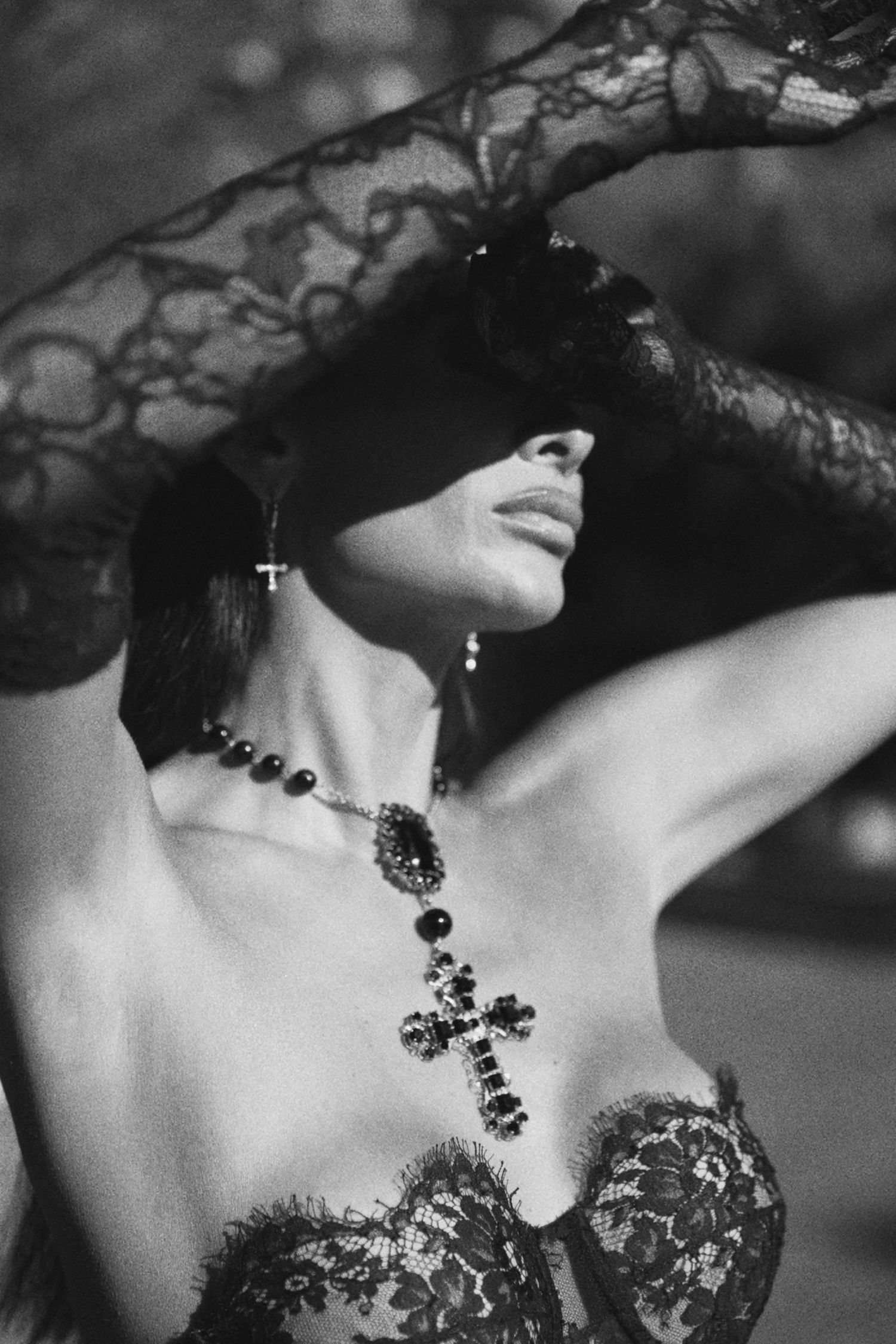 A dramatic black and white photo showing a gothic-style necklace with cross pendant against lace and corset details.