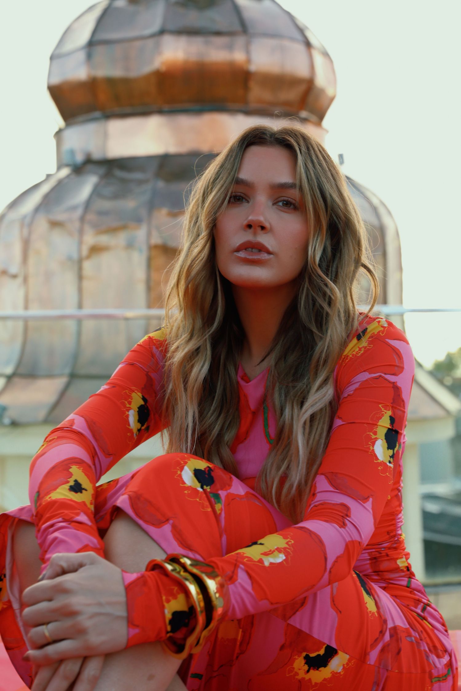 Model wears bright floral print dress against architectural dome background.