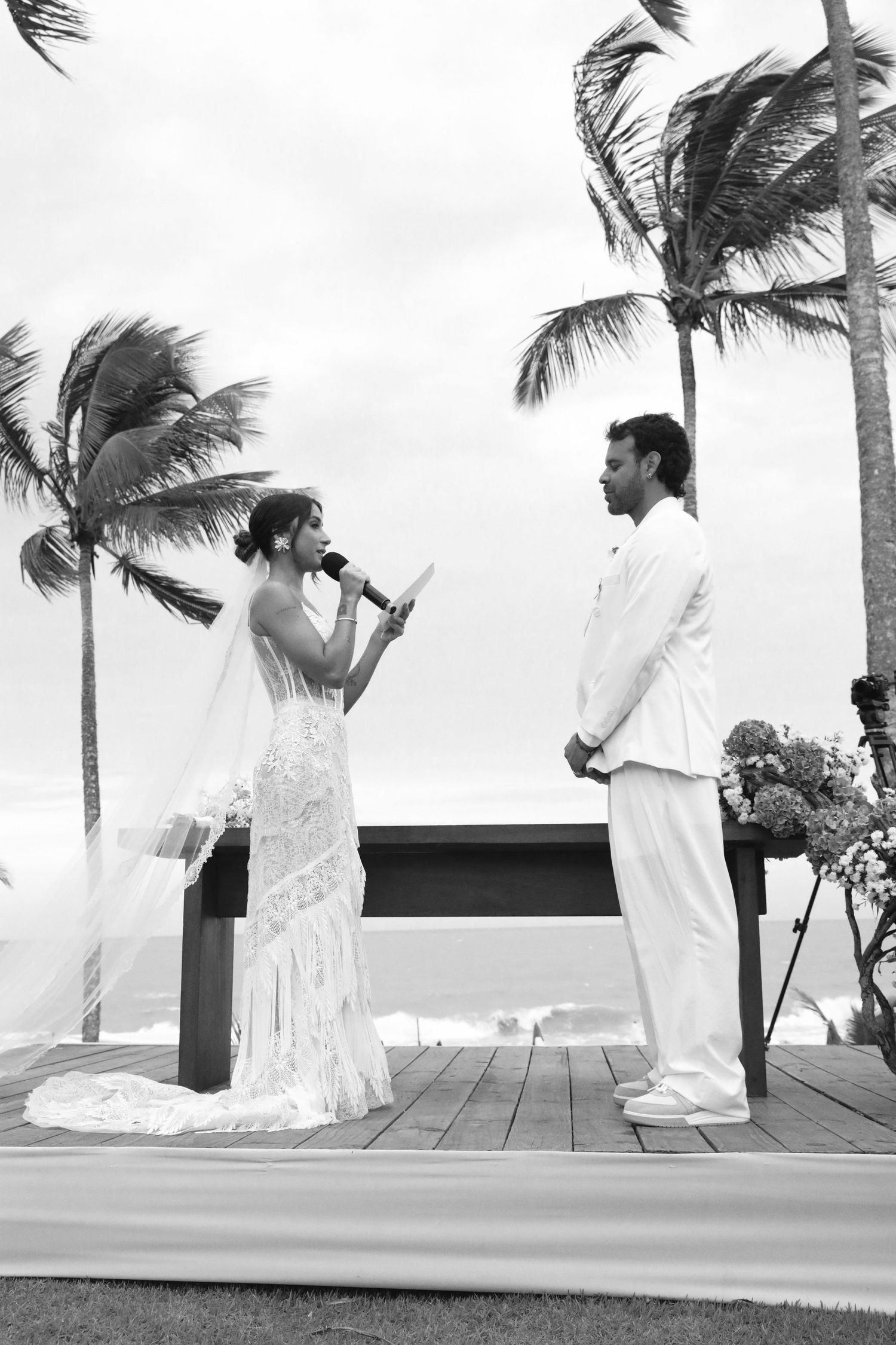A wedding ceremony taking place on a wooden deck with palm trees swaying in the tropical breeze.