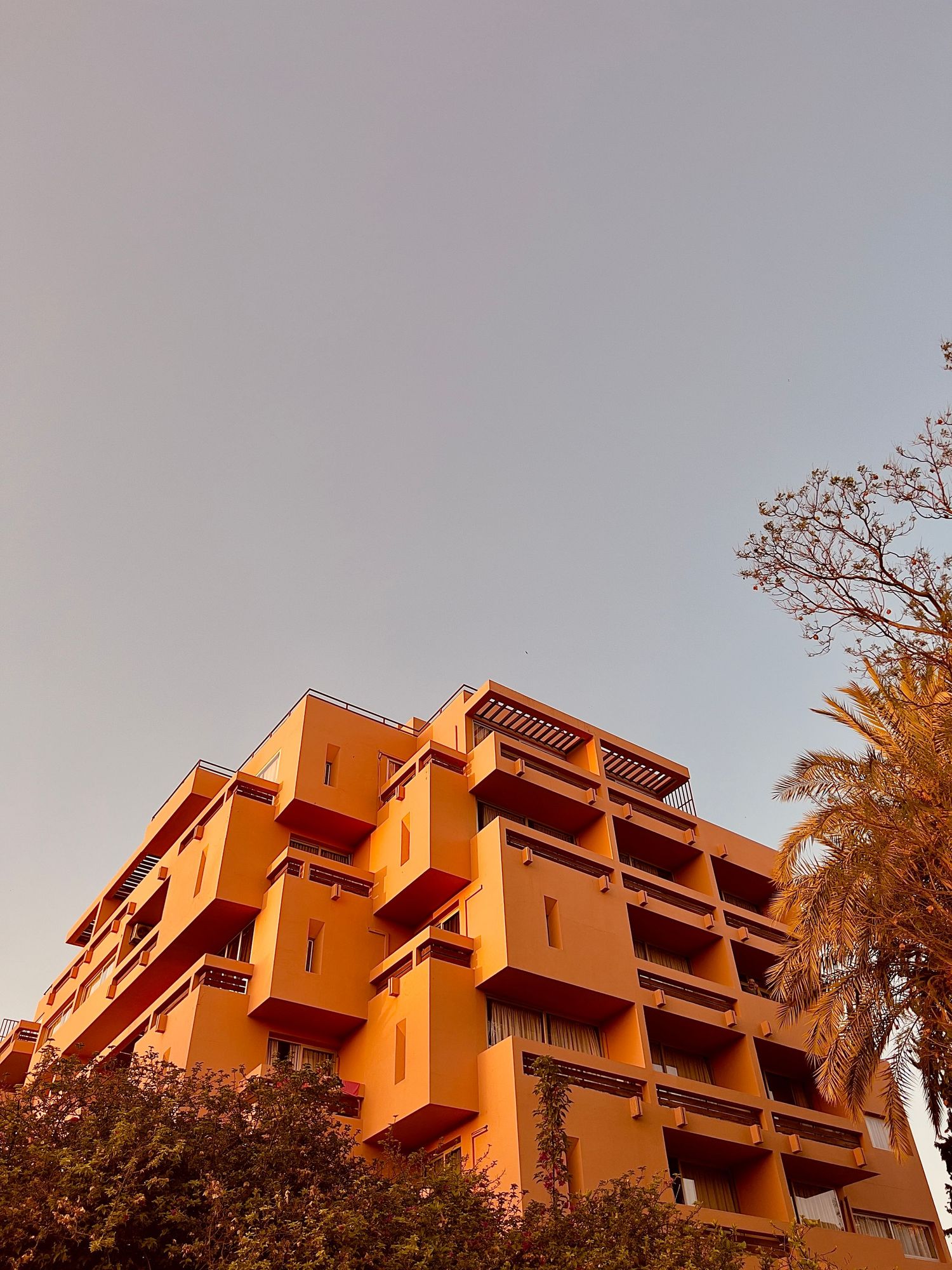 Orange terraced apartment building with staggered balconies photographed against a pale sky during sunset.