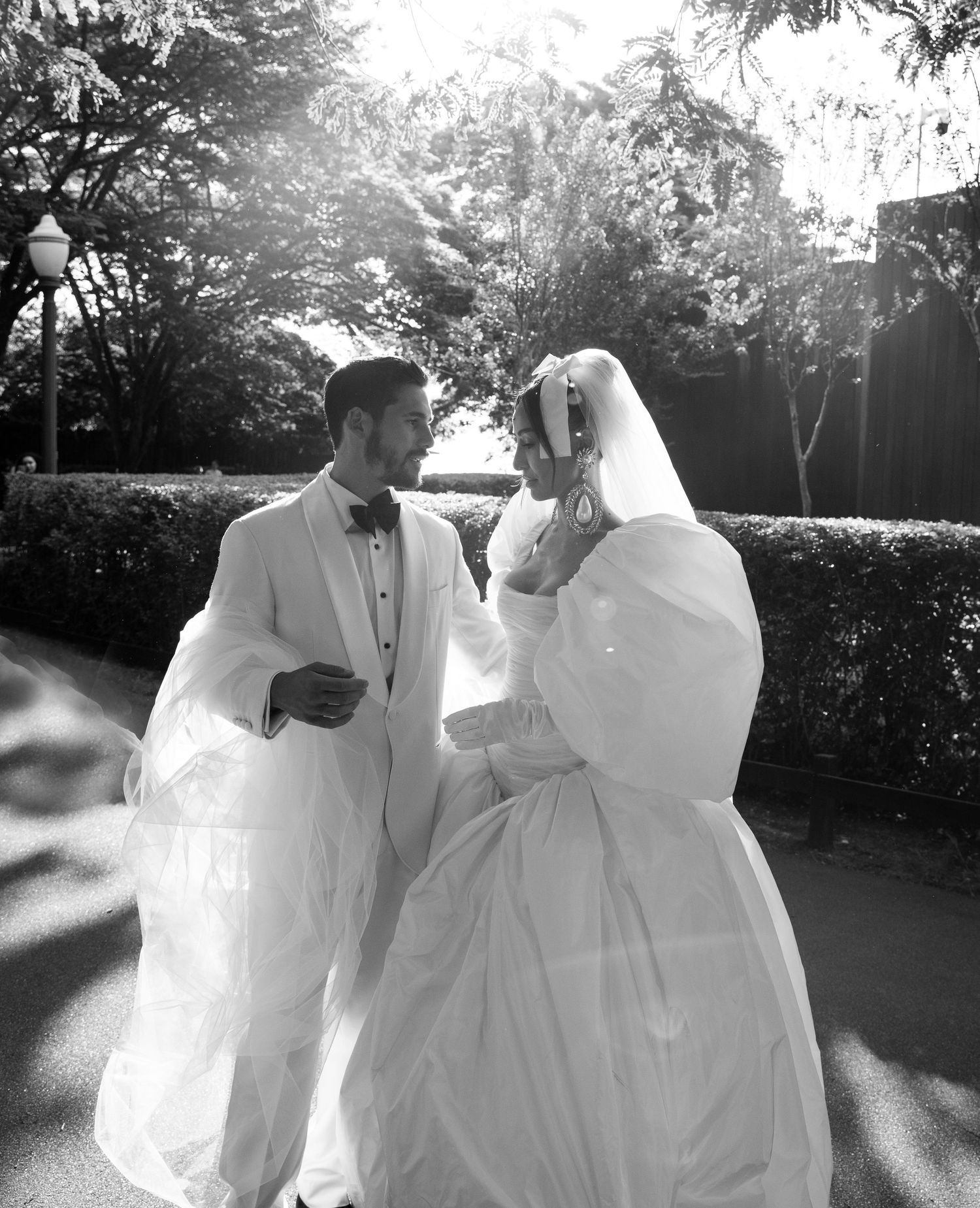 A black and white wedding photo showing a couple in white attire sharing a tender moment in a garden setting.