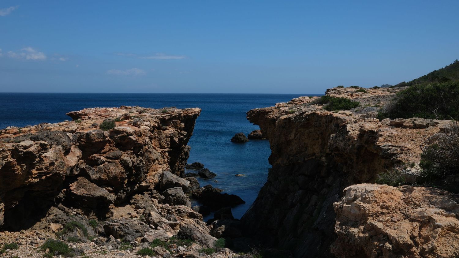 Rugged coastal cliffs and rocky outcrops overlooking the deep blue Mediterranean Sea on a sunny day.