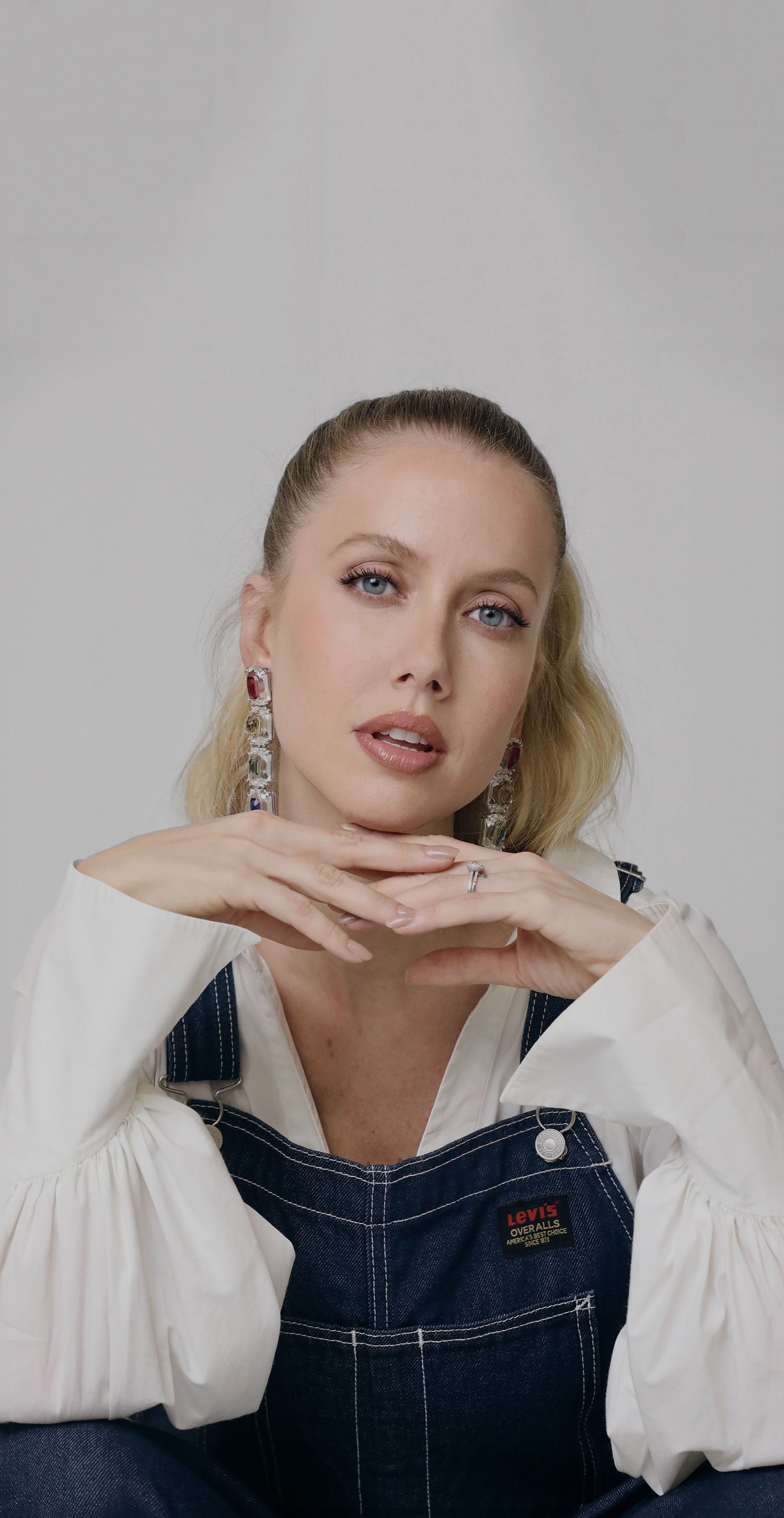 Portrait of model in white peasant blouse and denim overalls with statement earrings.
