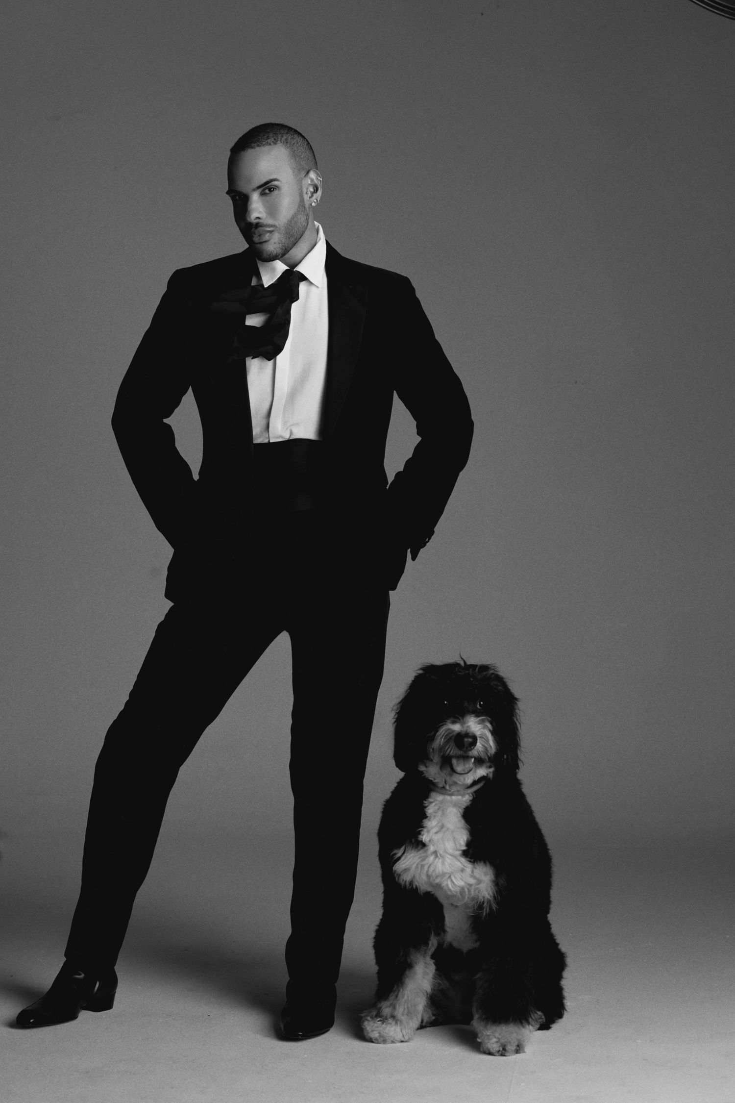 Formal black and white portrait of person in tuxedo standing with black and white dog.