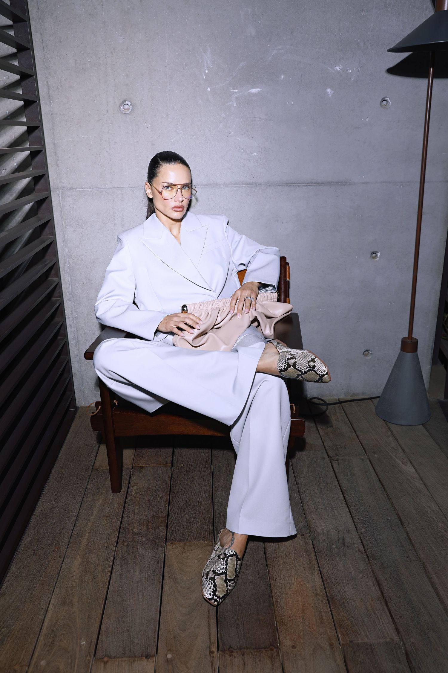 Person in white lab coat and glasses sitting on wooden bench in vintage studio setting.