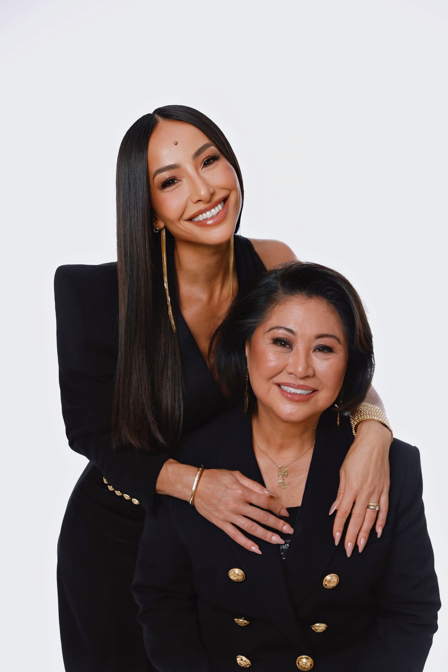 Studio portrait of two women in black outfits sharing warm embrace against white background.