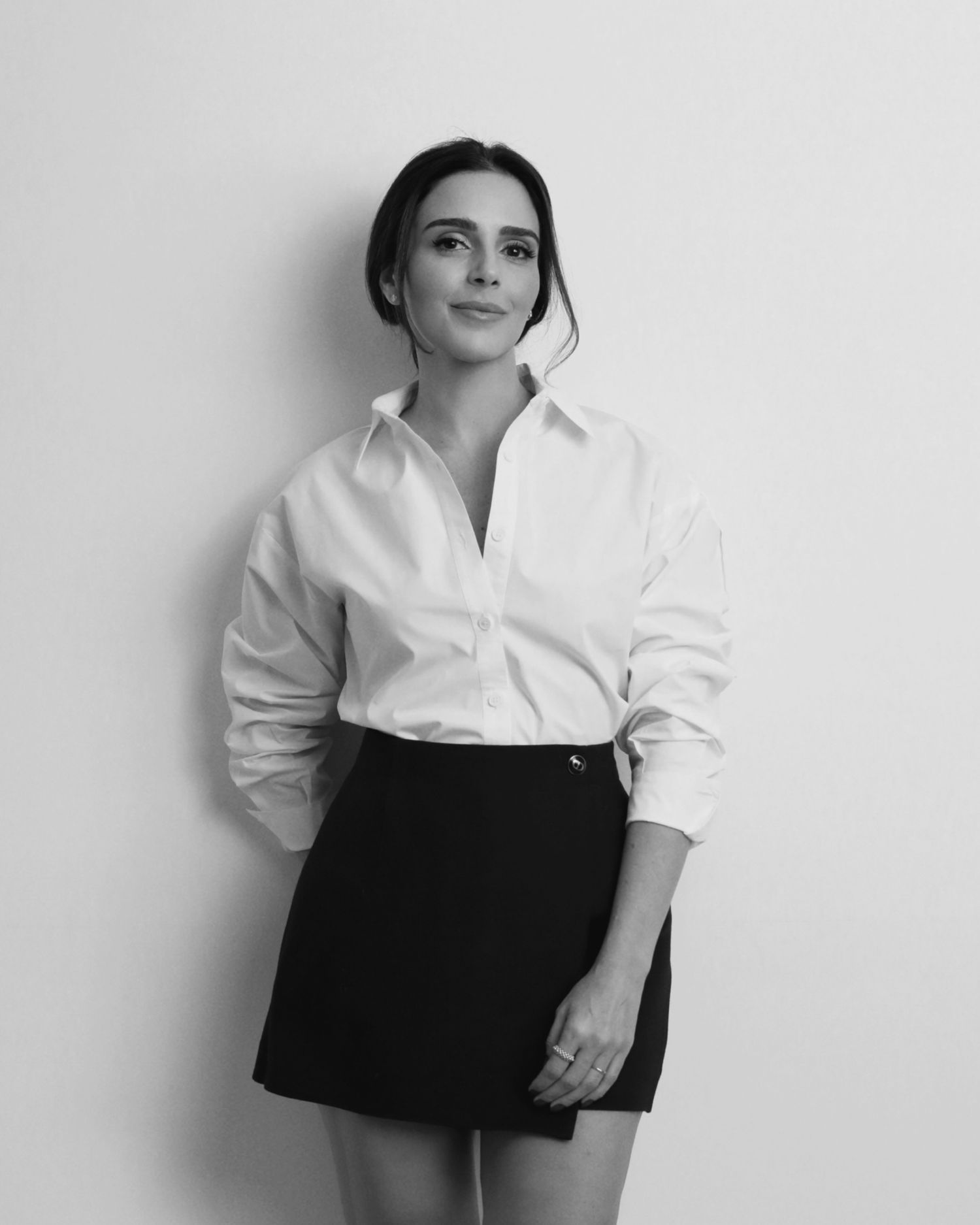 A minimalist portrait of a person in crisp white shirt and black mini skirt against white background.