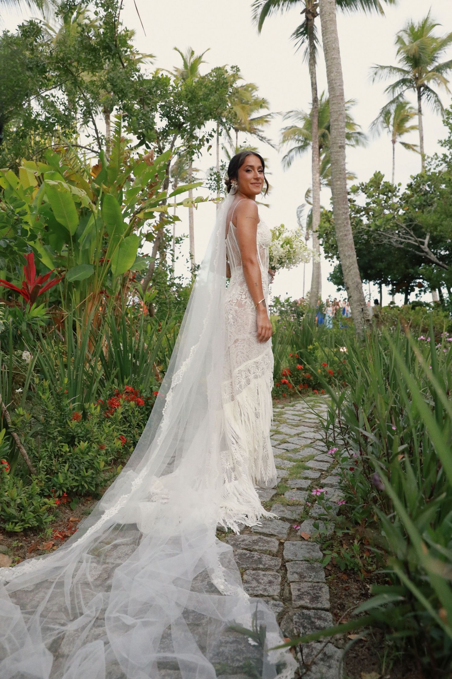 A stunning white lace wedding gown with flowing cathedral veil photographed in a tropical garden with palm trees.