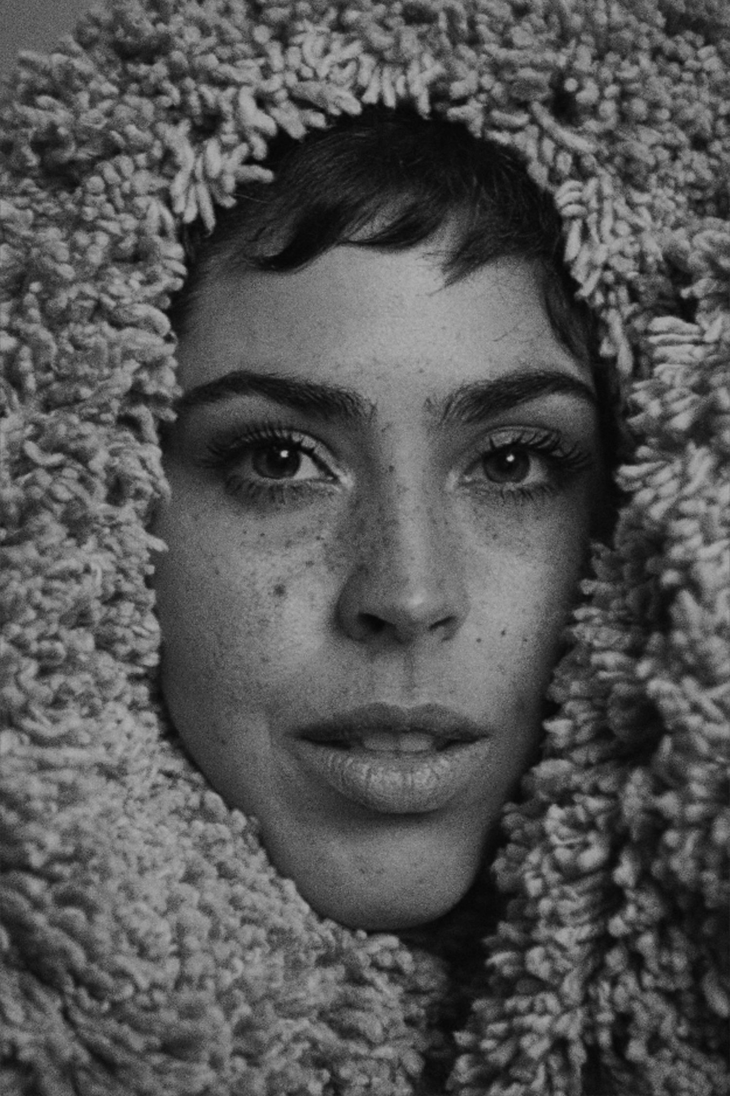 Artistic black and white portrait showing face framed by textured fabric.