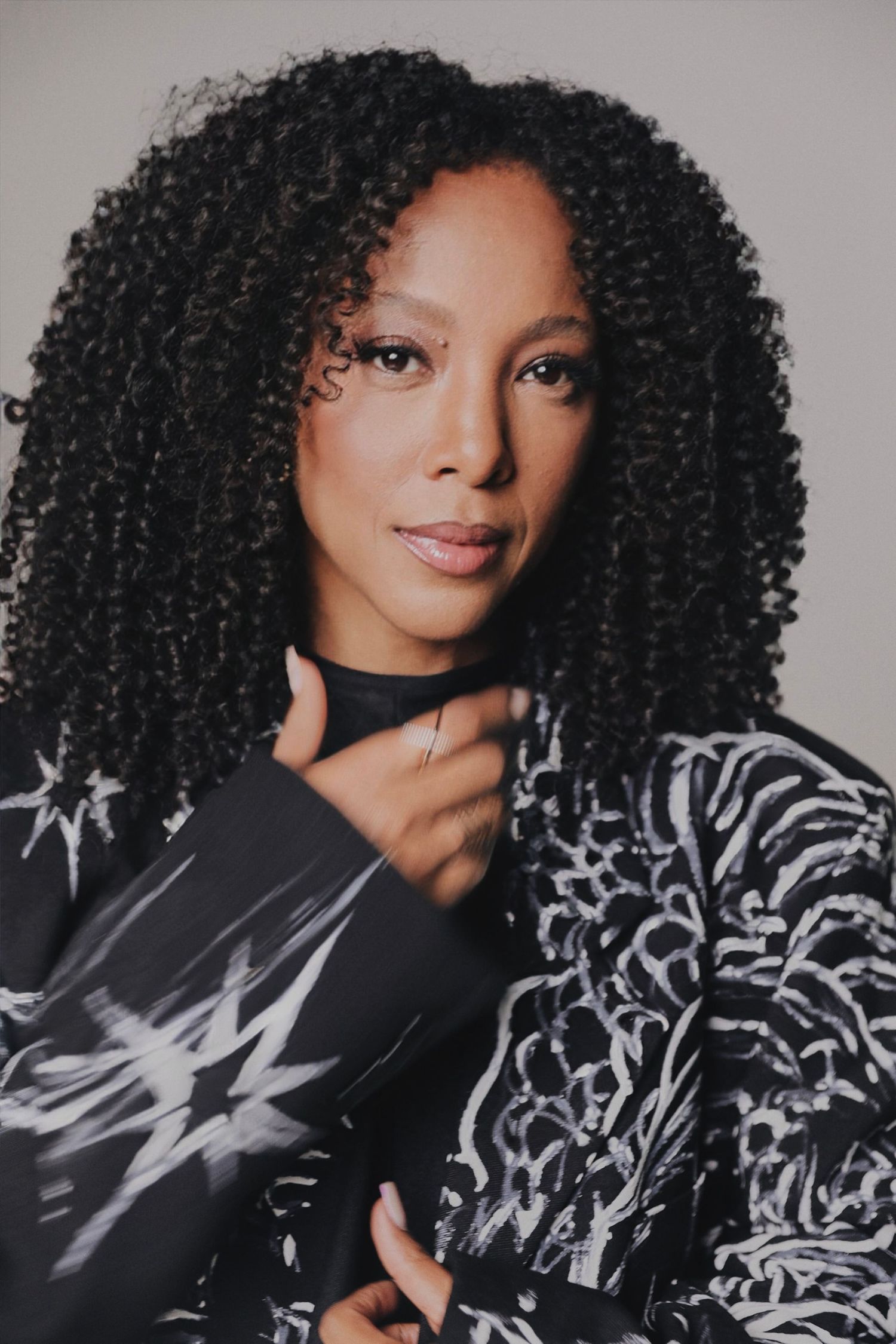 A portrait featuring natural curly hair and a graphic printed top with choker detail.