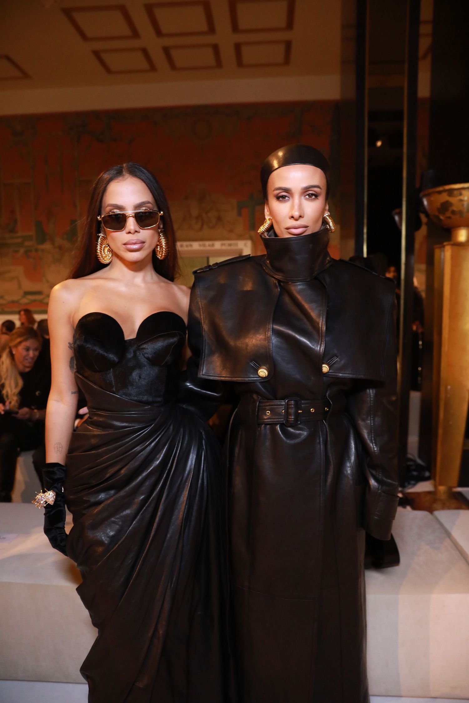 Two people pose in black formal wear, one in a strapless gown and another in a structured coat.