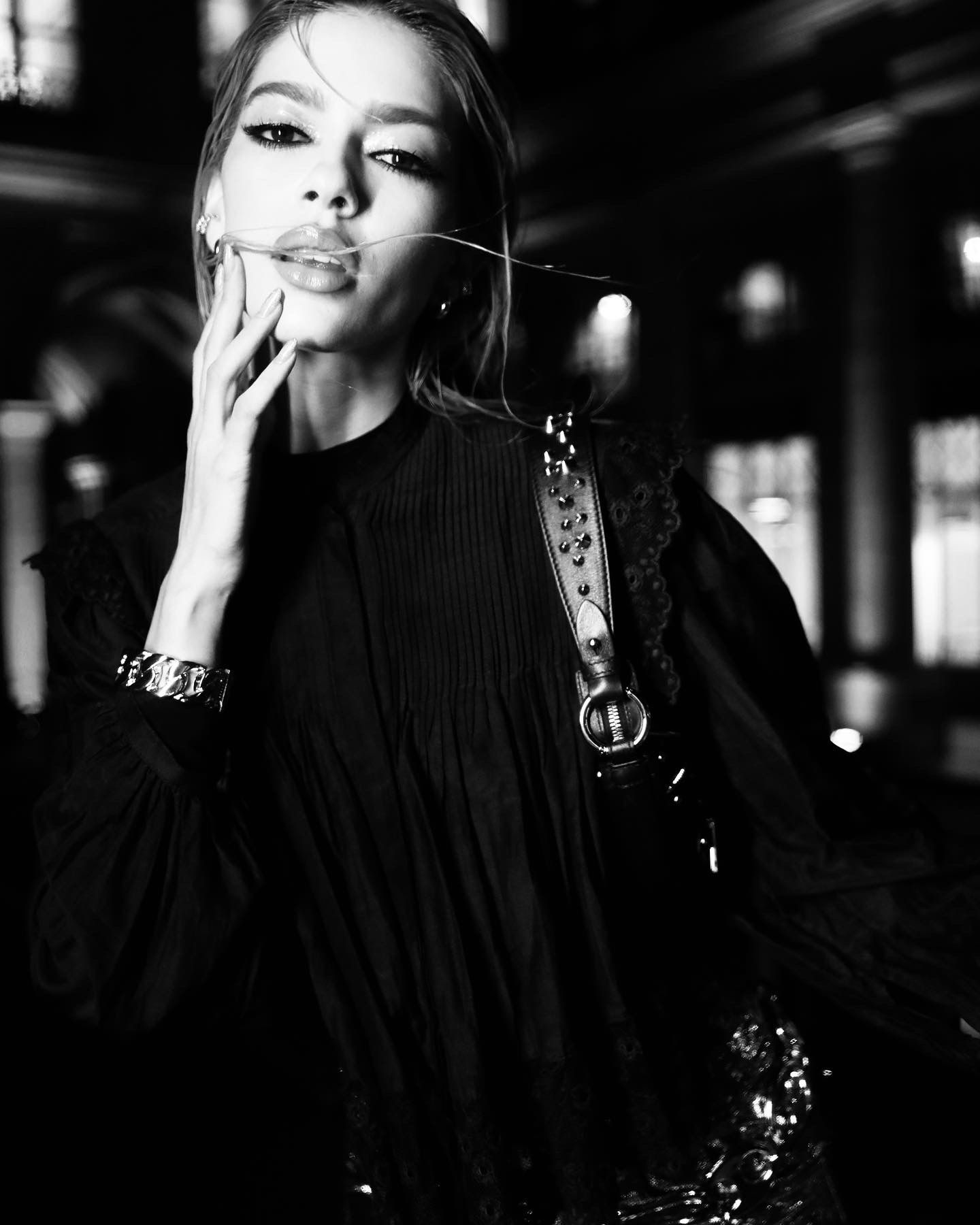 Dramatic black and white fashion portrait of a person in dark clothing with statement jewelry.