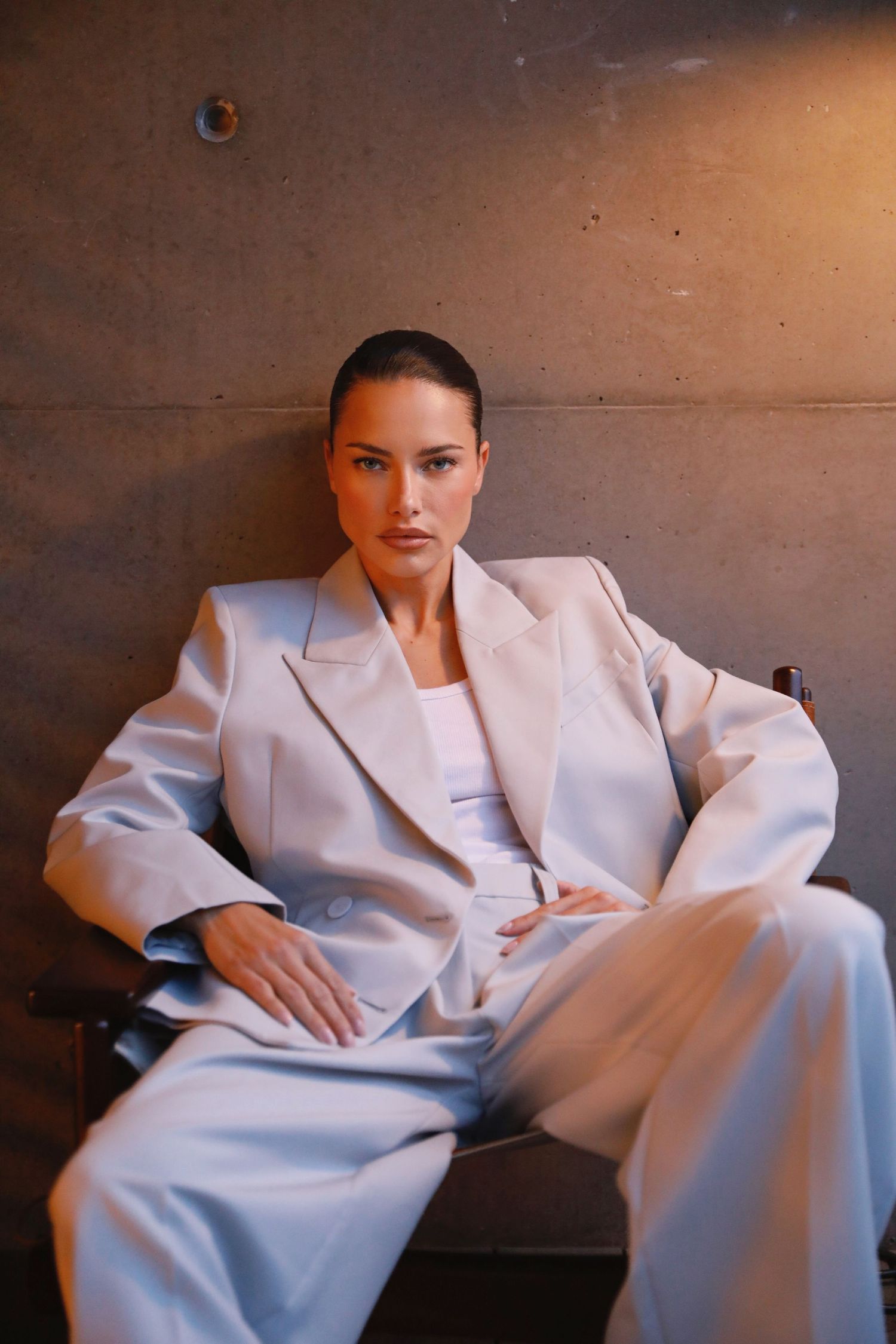 A person in a white tailored suit poses against a brown wall in a series of minimalist fashion shots.