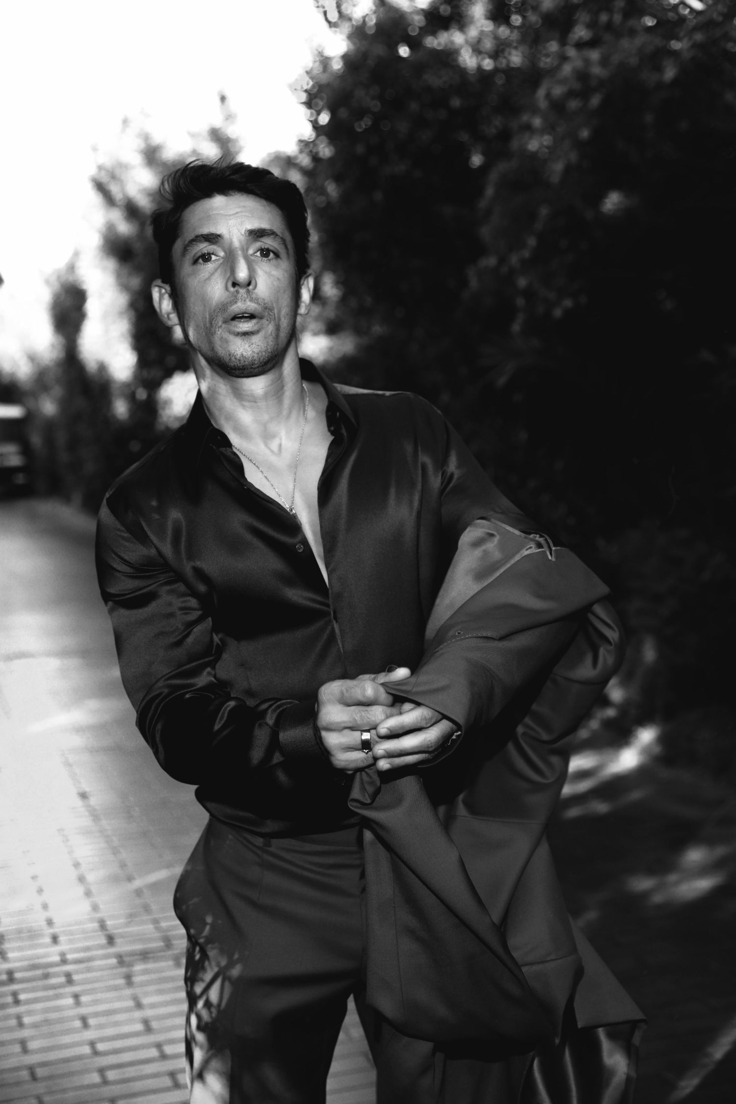 A black and white photo of a person in silk clothing standing on a brick pathway outdoors.