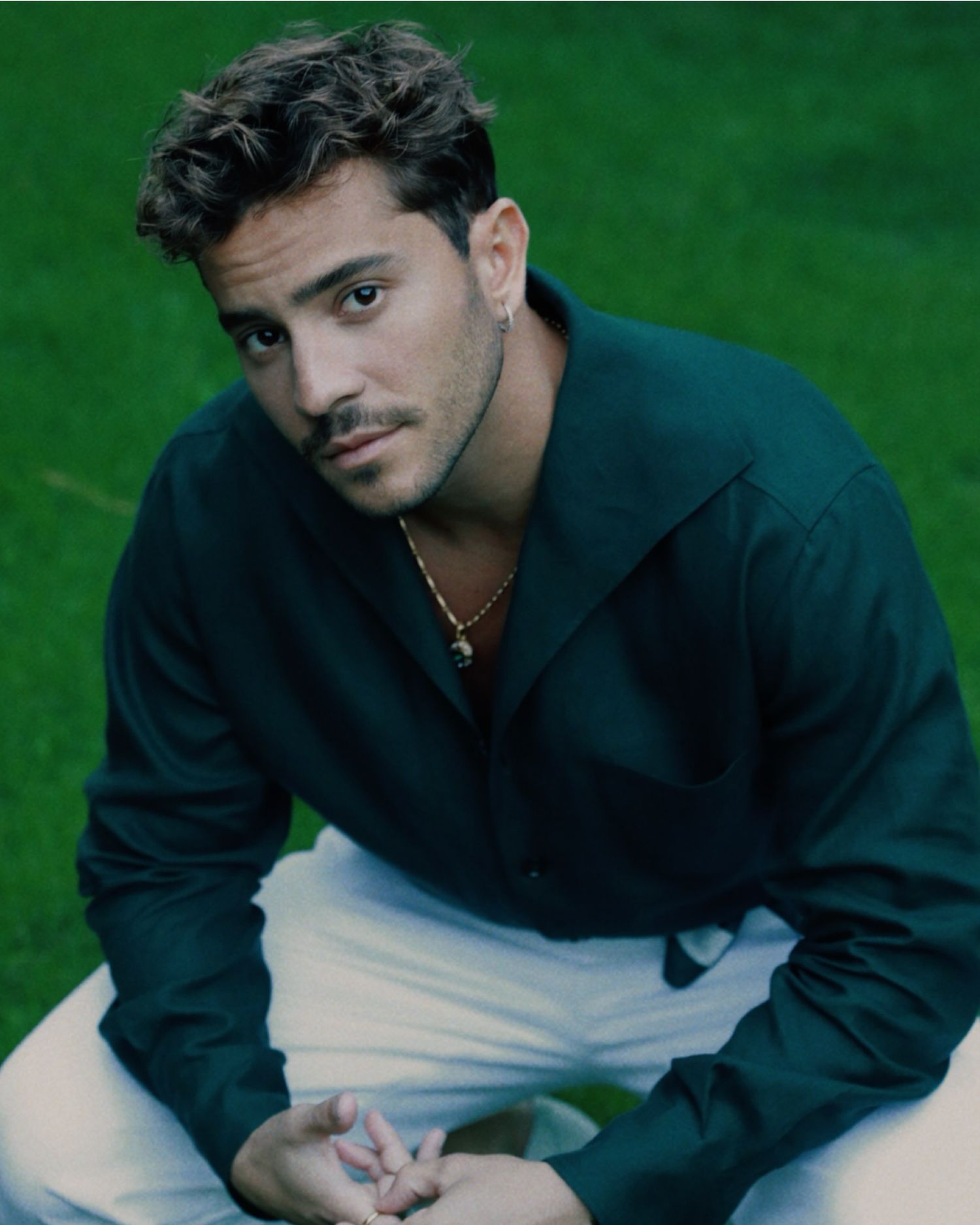 Portrait of someone wearing a navy blue collared jacket and white pants against a green background.