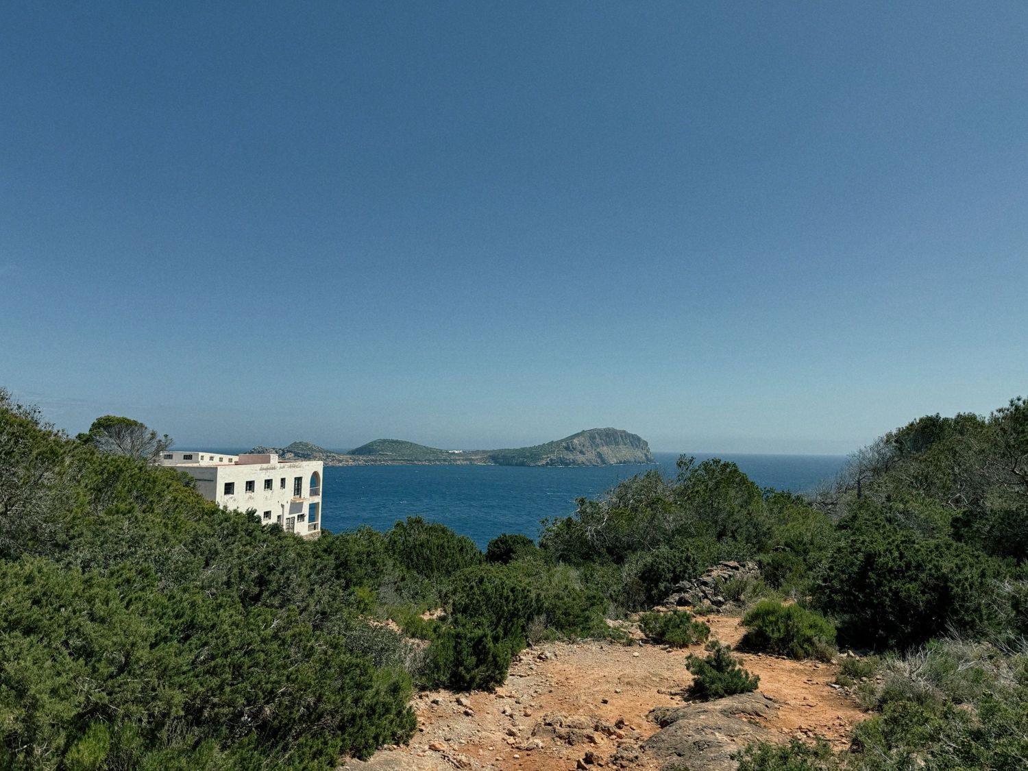 A panoramic coastal view showing rocky cliffs, blue ocean waters, and lush greenery under a clear sky.