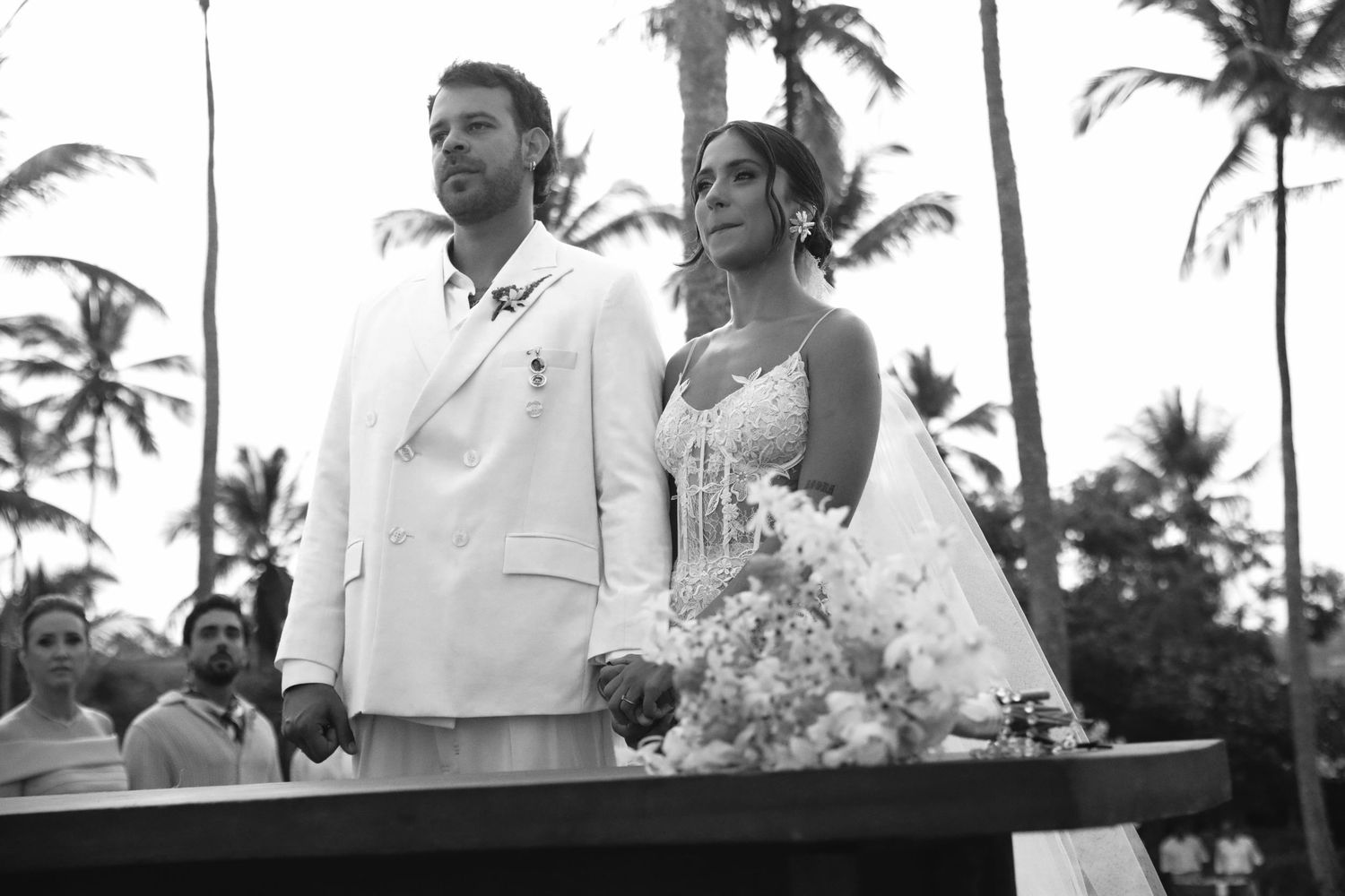 A black and white photo of a tropical beach wedding ceremony with palm trees in the background.
