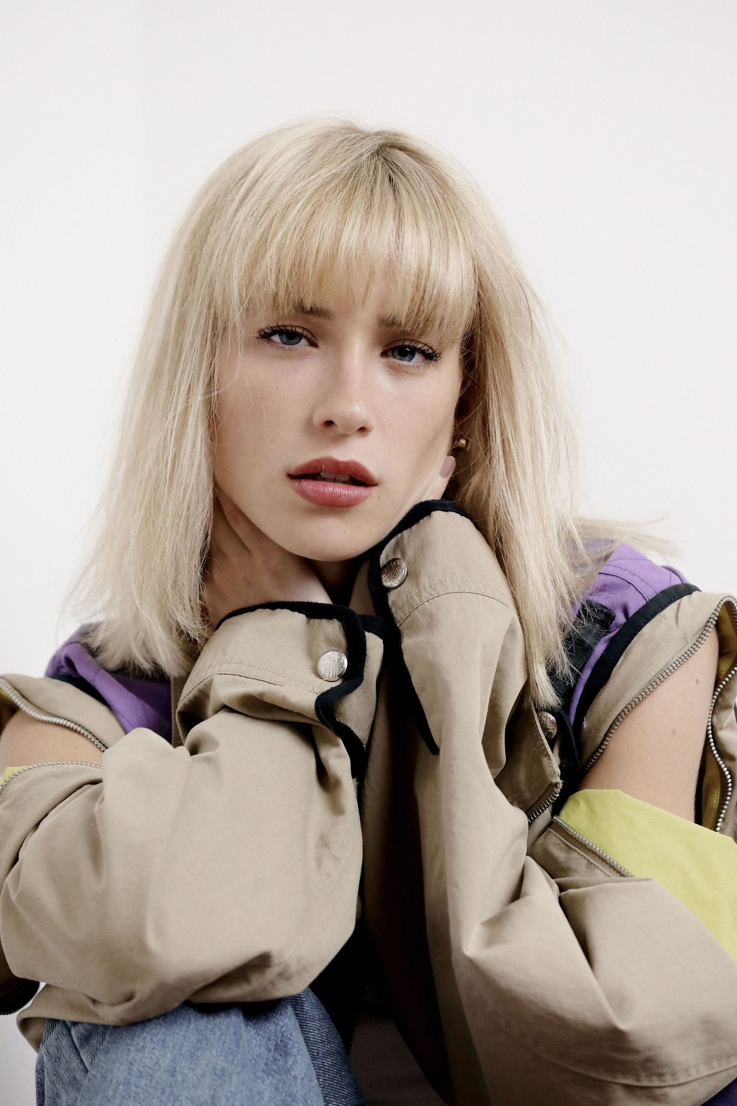 Fashion portrait featuring a beige jacket with purple and yellow accents paired with denim against a light background.