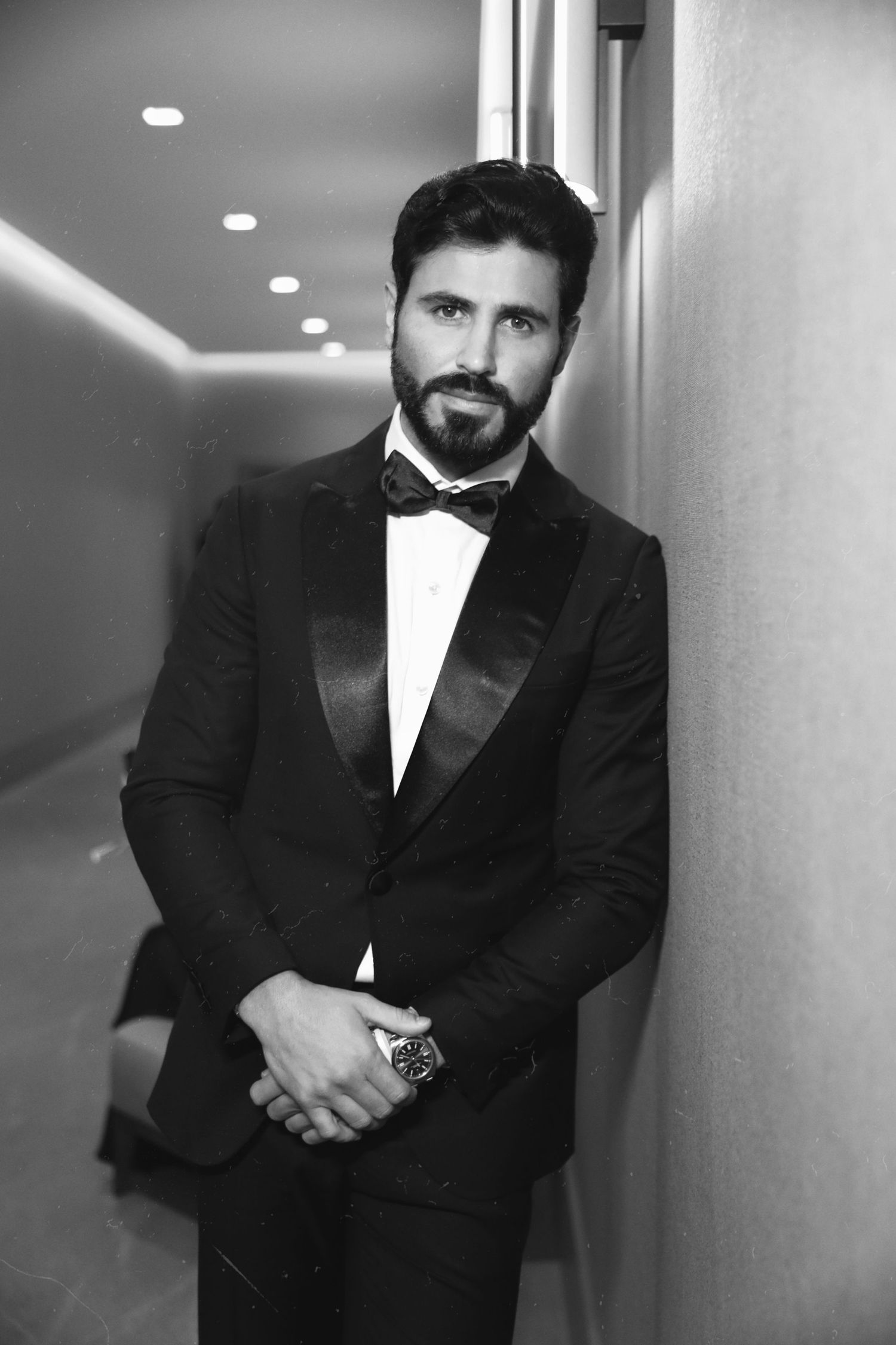 Black and white hallway portrait of person wearing classic tuxedo and bowtie.