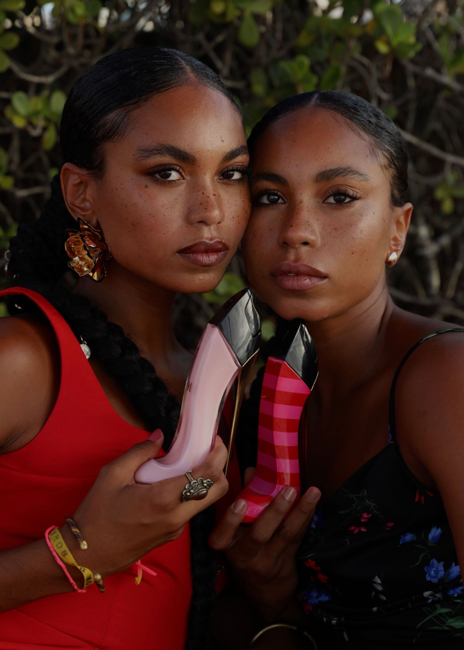 Two models showcase Carolina Herrera fragrance in elegant dresses against natural backdrop.