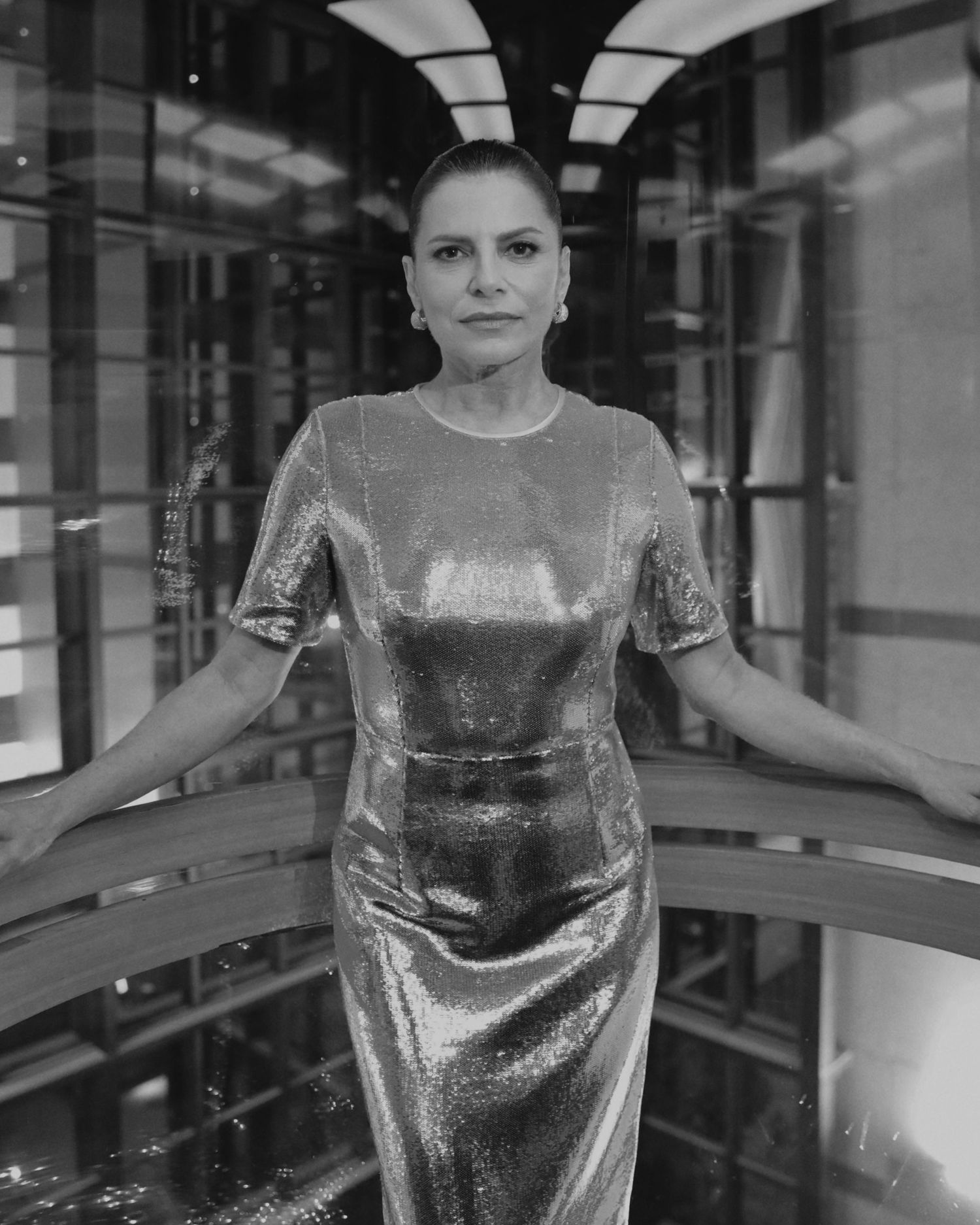 A person poses in a silver metallic fitted dress in an elegant indoor setting with dramatic lighting.