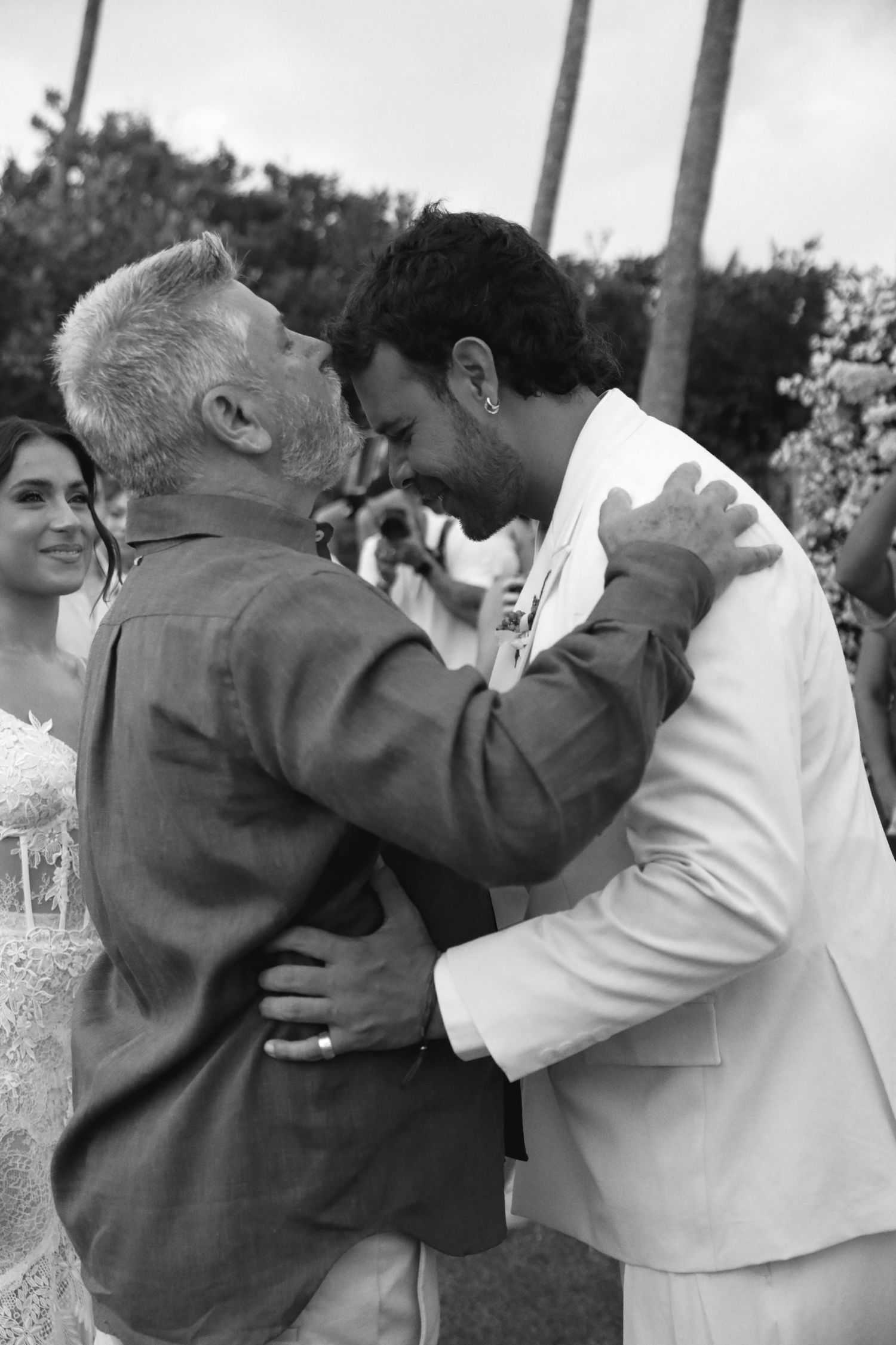 A heartfelt embrace between two people at an outdoor celebration wearing contrasting light and dark outfits.