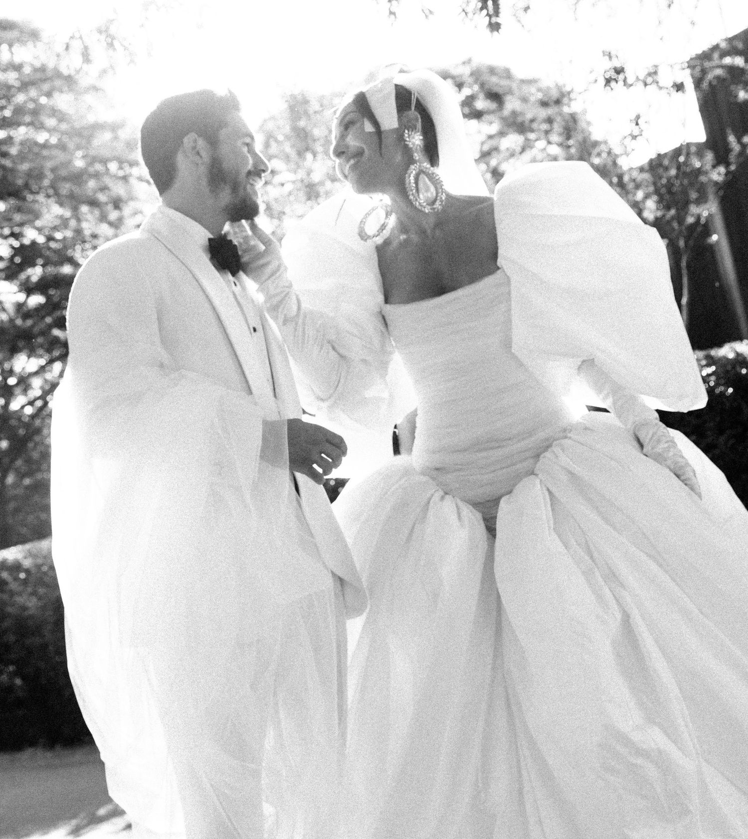 Elegant wedding couple in all-white attire smiling at each other during their outdoor celebration.