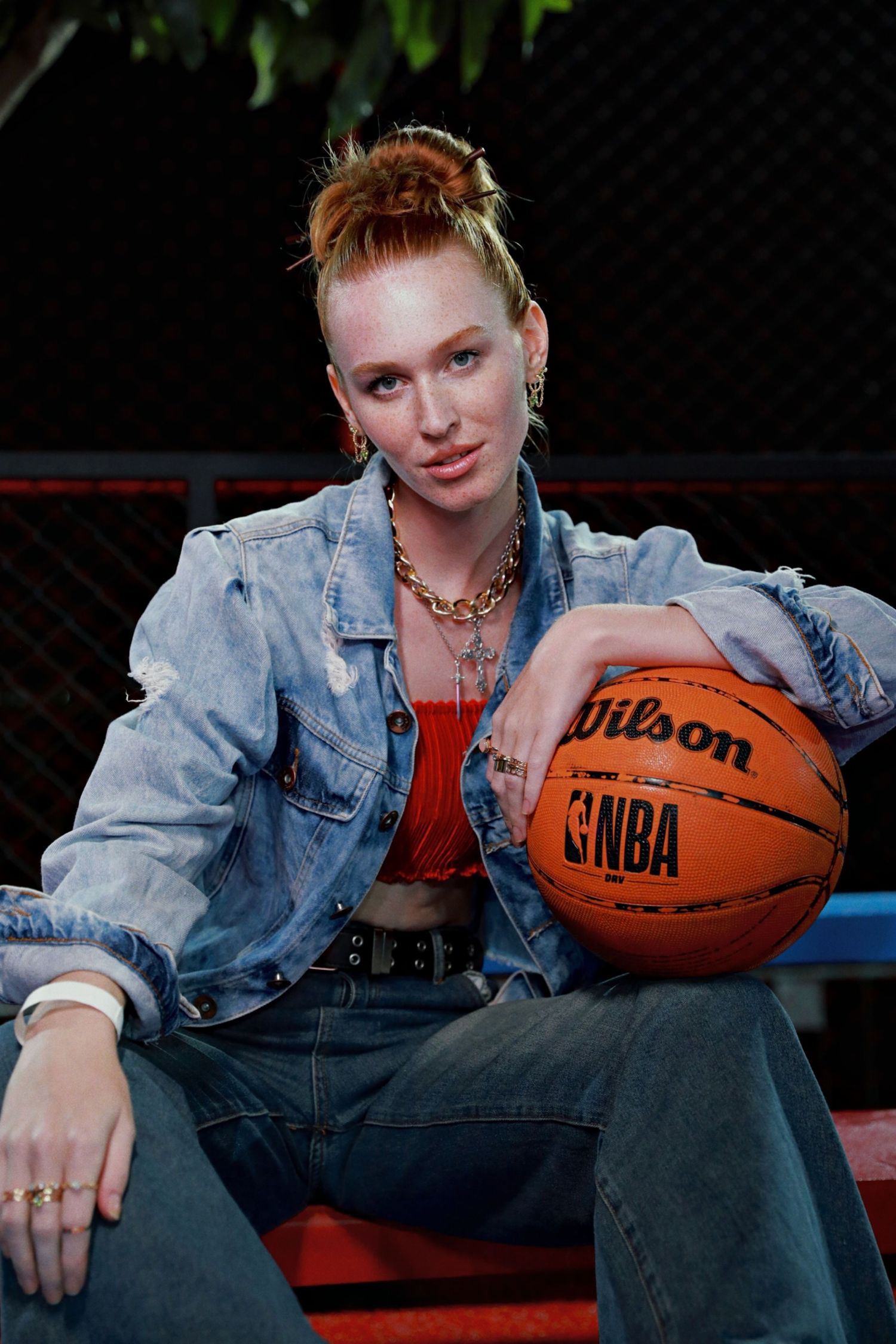 A casual street style portrait with someone posing with a basketball in denim and red top.