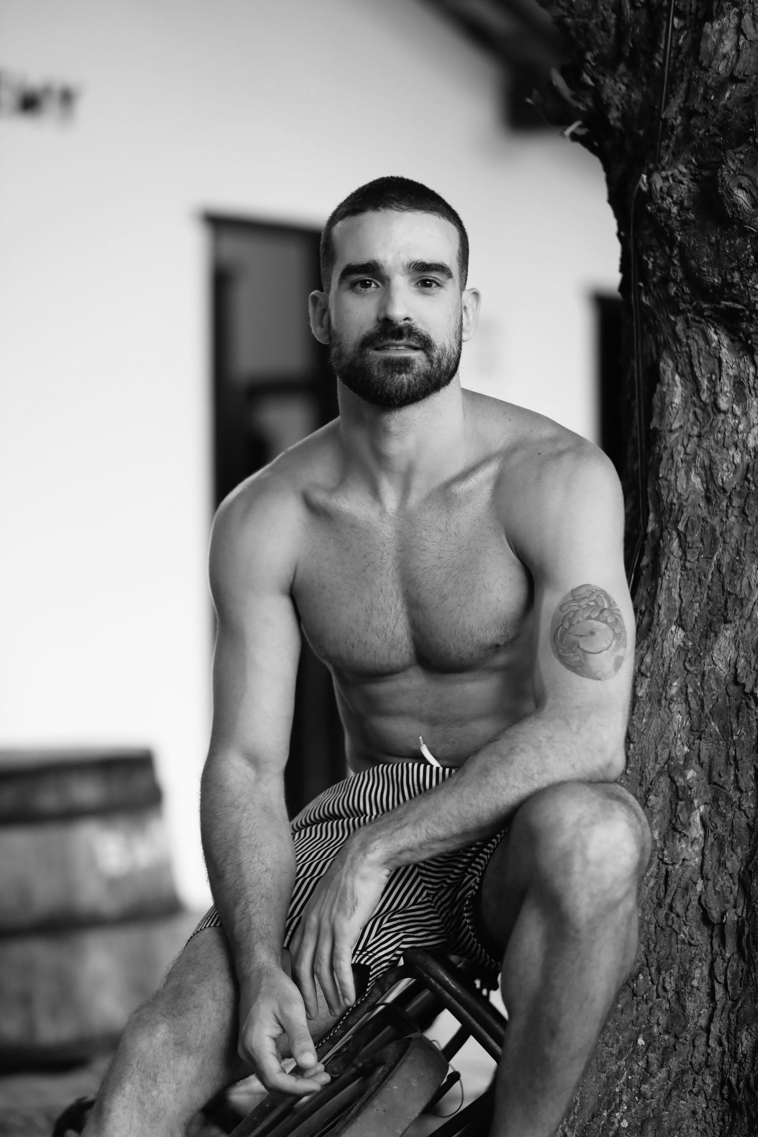 Black and white outdoor portrait of a shirtless person with tattoos.