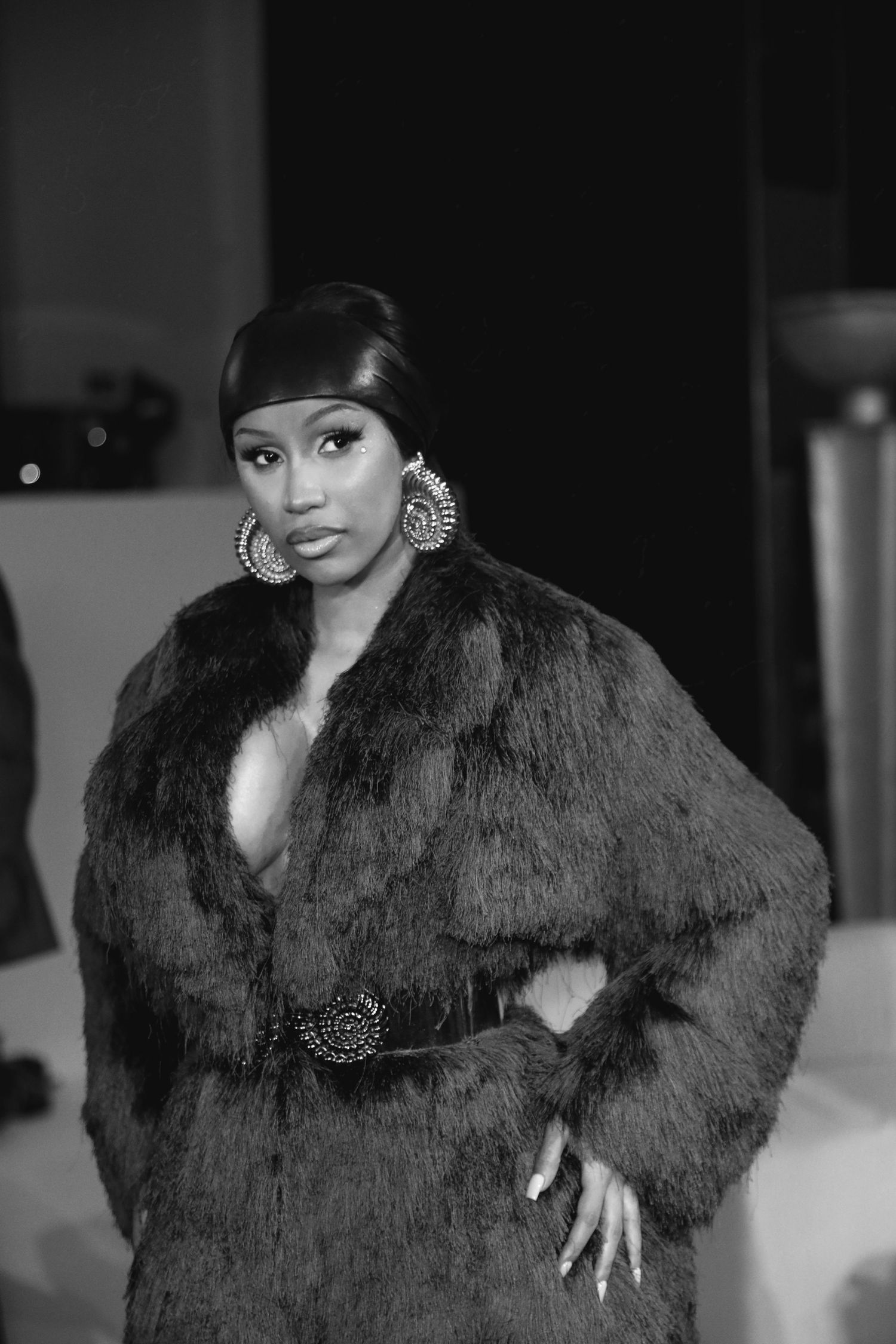 Glamorous photo in black and white showing a woman in a luxurious fur coat with statement earrings and ornate belt.
