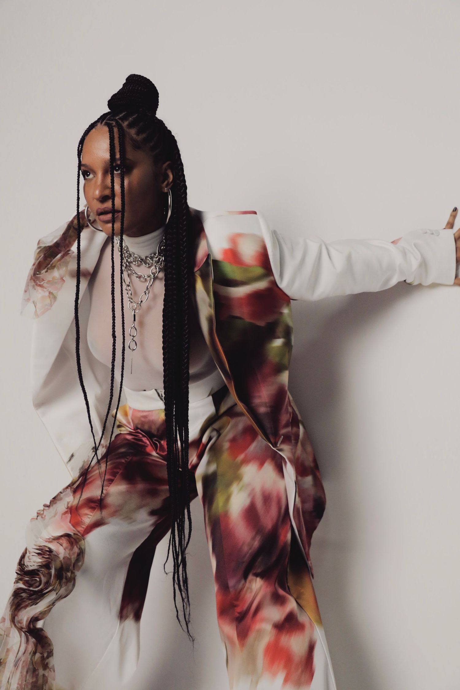 Model in floral print outfit with long braids poses artistically against light background.
