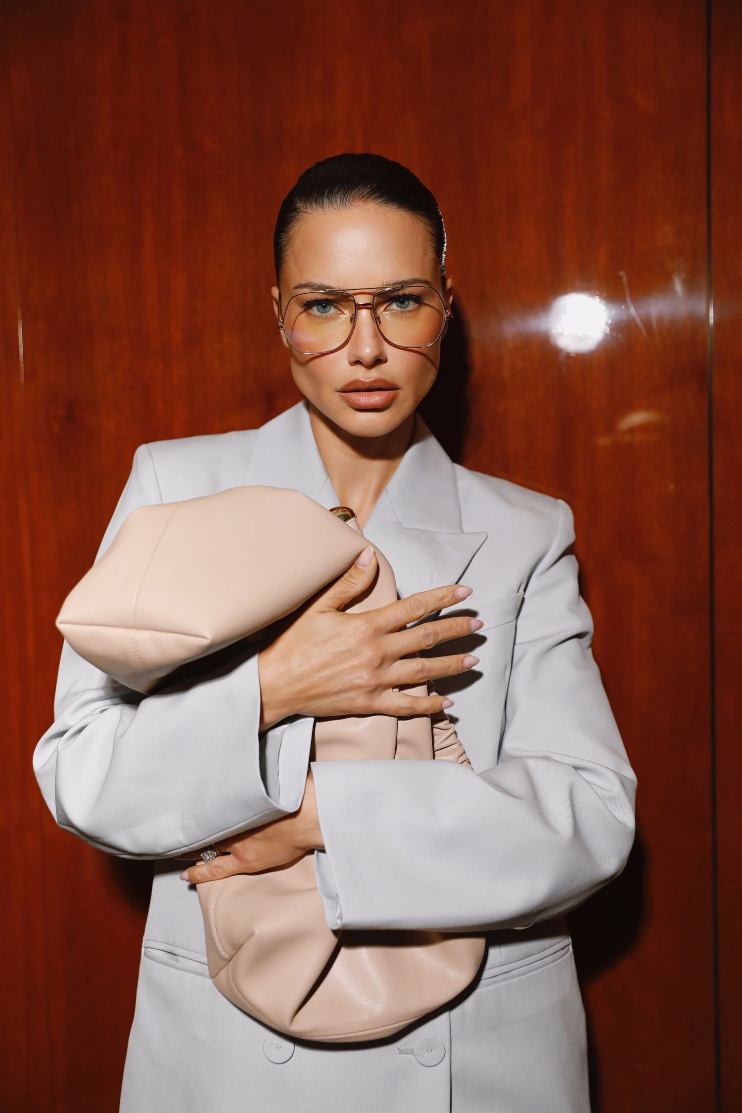 Four sequential photos show someone in a light gray suit jacket holding and embracing a nude-colored pillow against a wood wall.