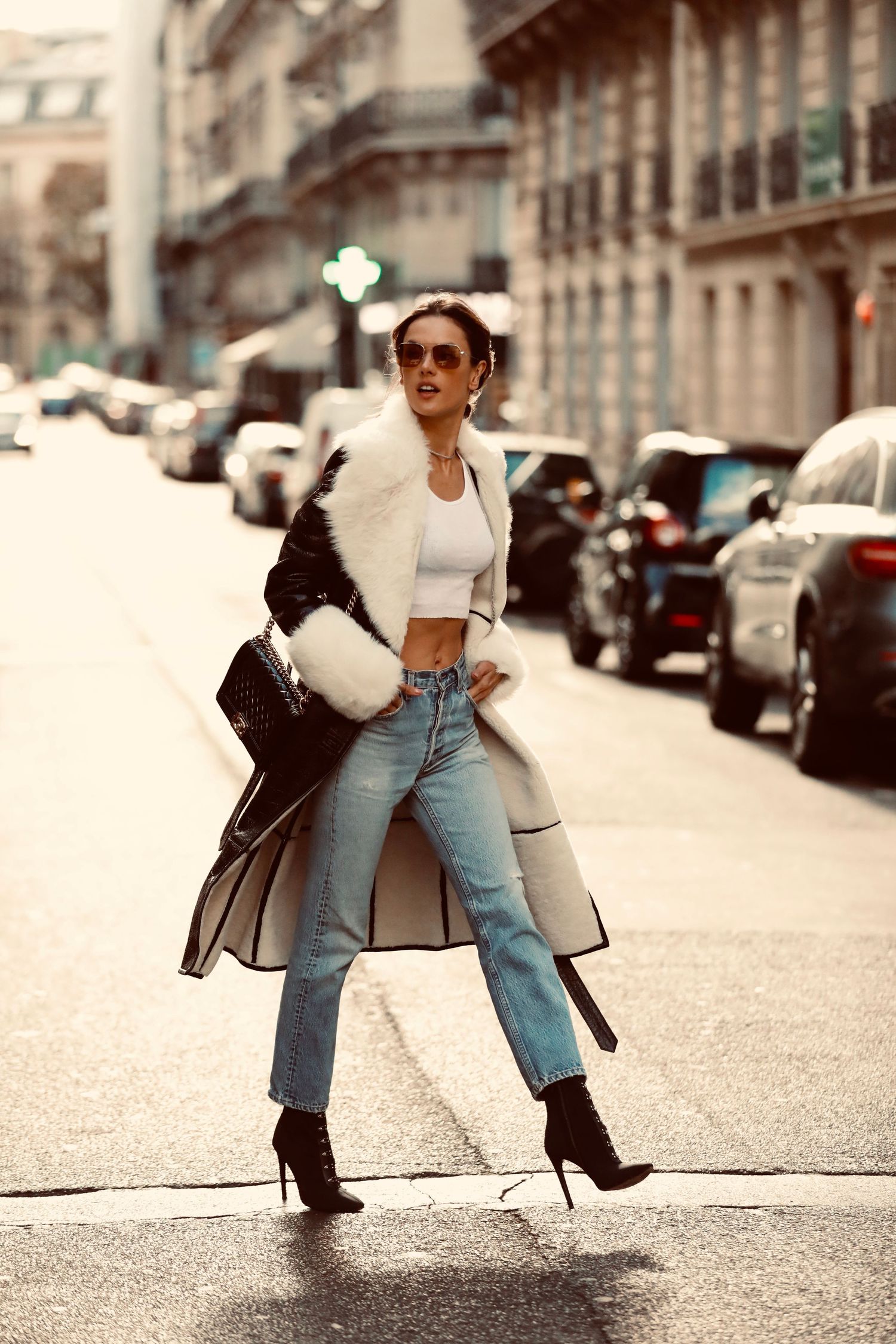 Fashionable street style with crop top, long coat, high waist jeans and ankle boots on a city street in Paris.