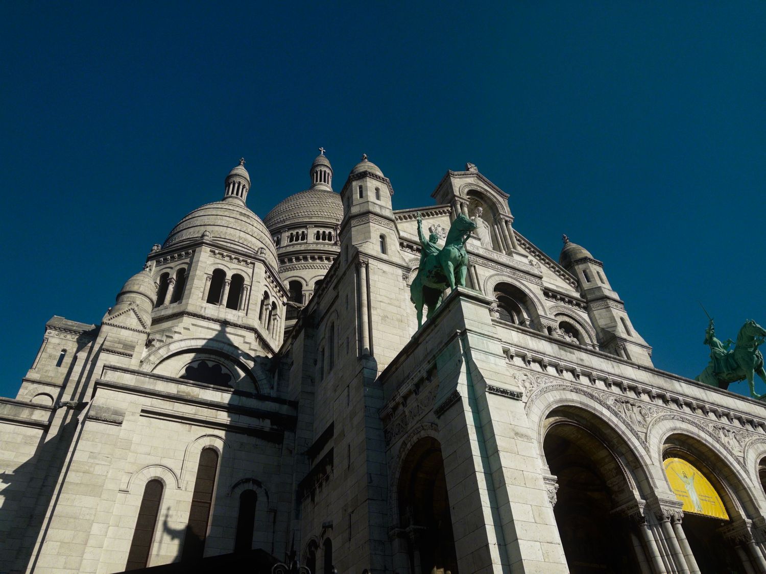 Architectural details of the iconic Sacre-Coeur Basilica in Paris showing its white stone domes against a blue sky.