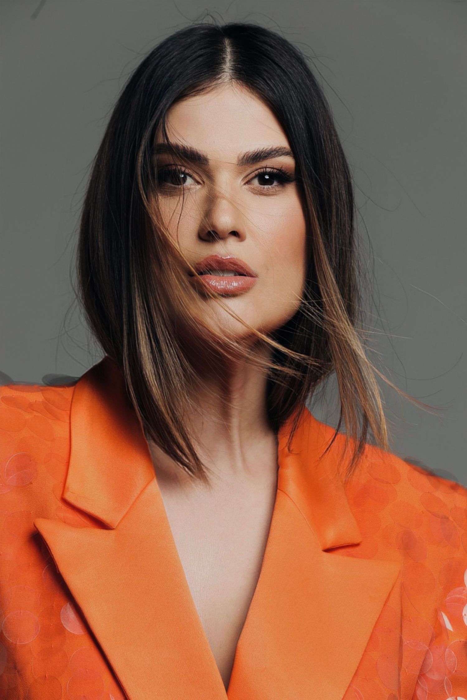 A fashion portrait featuring a vibrant orange blazer and sleek shoulder-length hair.