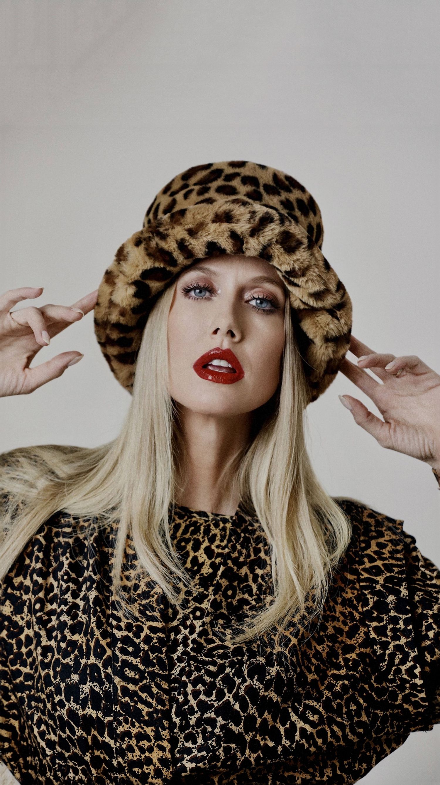 Fashion model wearing leopard print hat and matching blouse poses against white background with red lipstick.