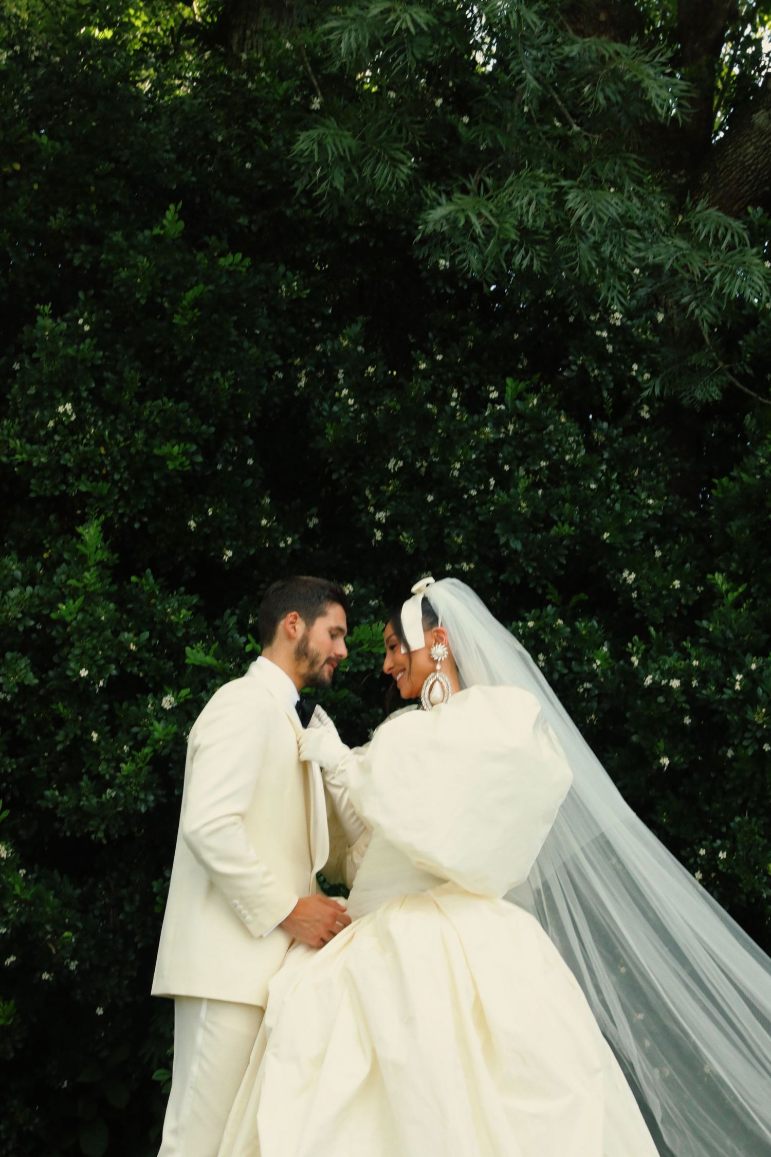 An intimate wedding portrait of a couple in white against lush green foliage.
