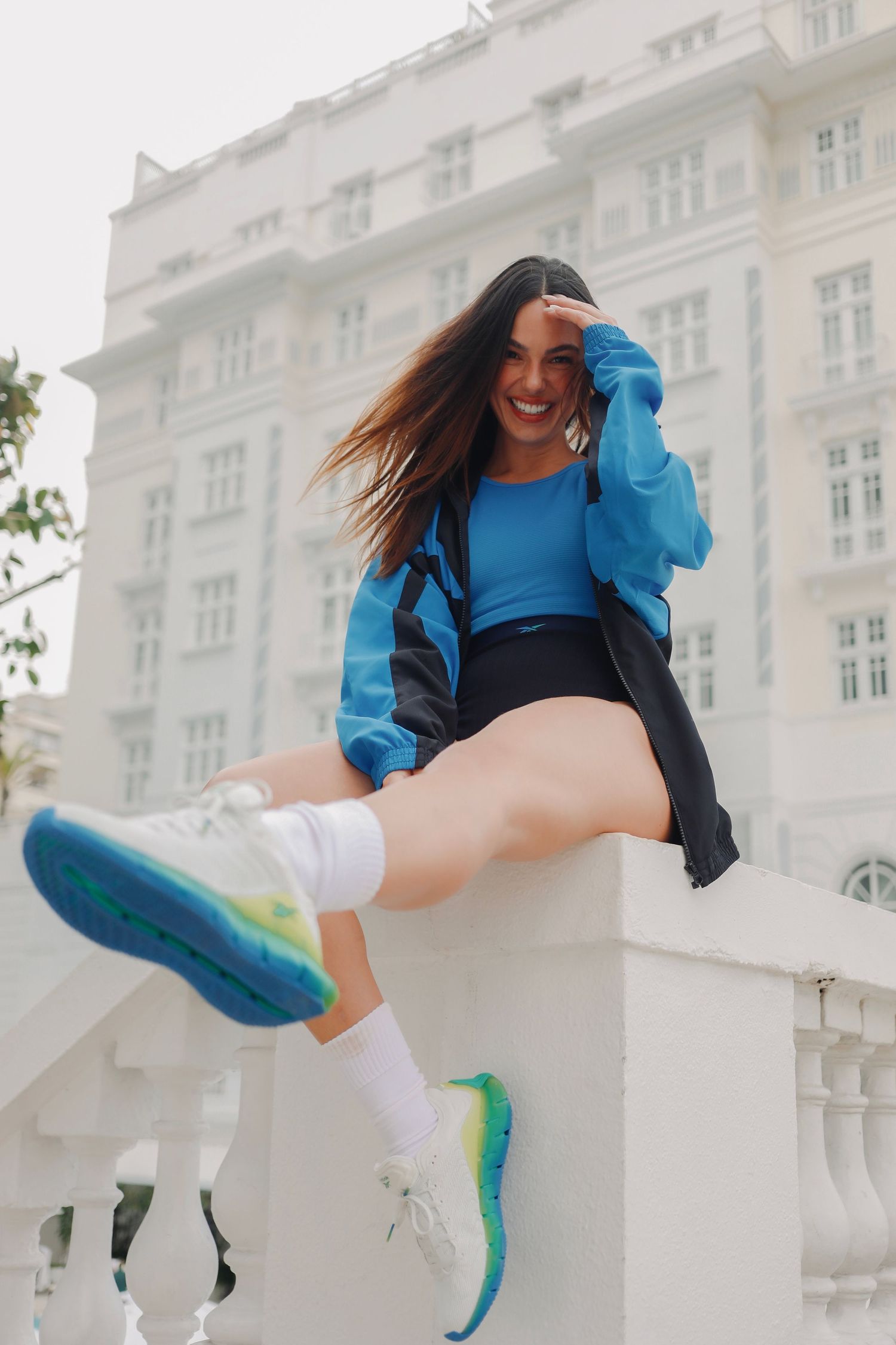 Person in bright blue outfit jumping playfully on white stone balcony in dynamic fashion pose.