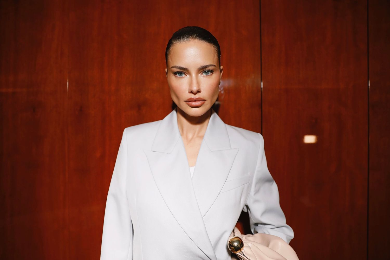 A person in a crisp white blazer poses confidently against a wooden paneled wall.