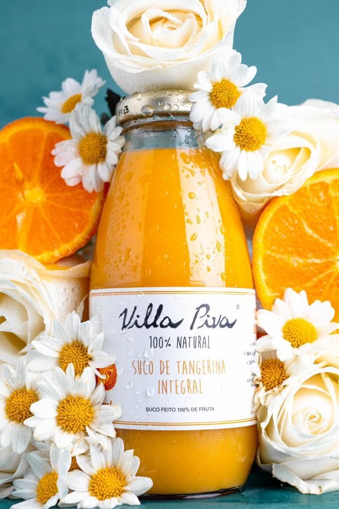 Bottle of Villa Para orange juice surrounded by fresh oranges, white roses and daisies on turquoise background.