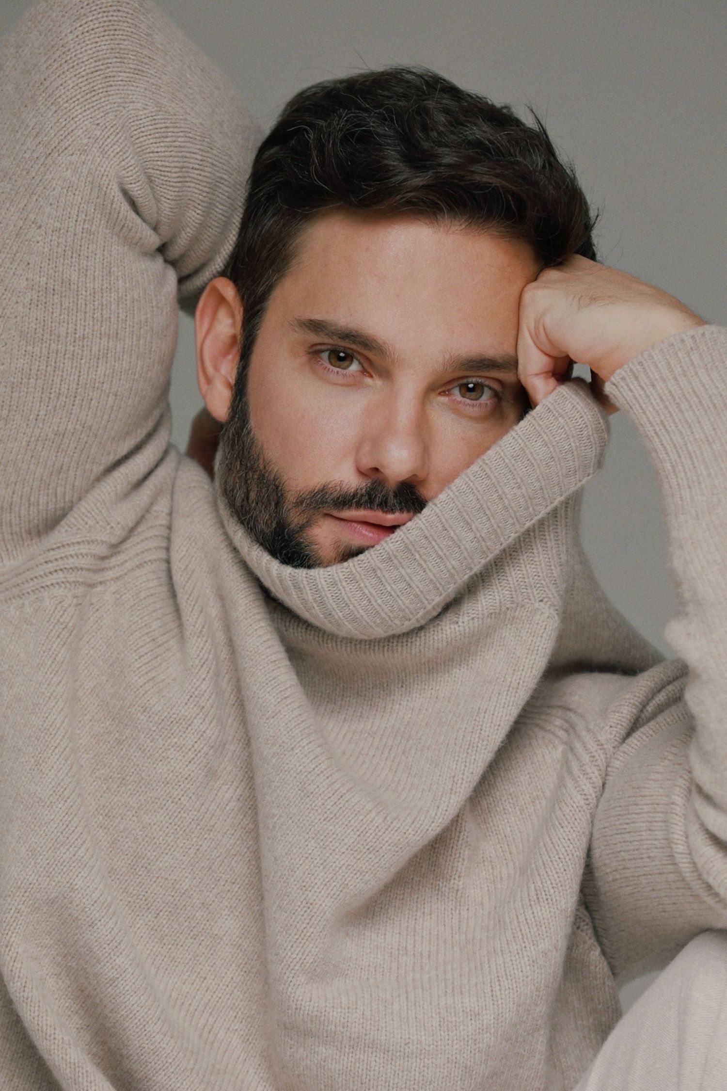 Close-up portrait of person in beige turtleneck sweater against gray background.