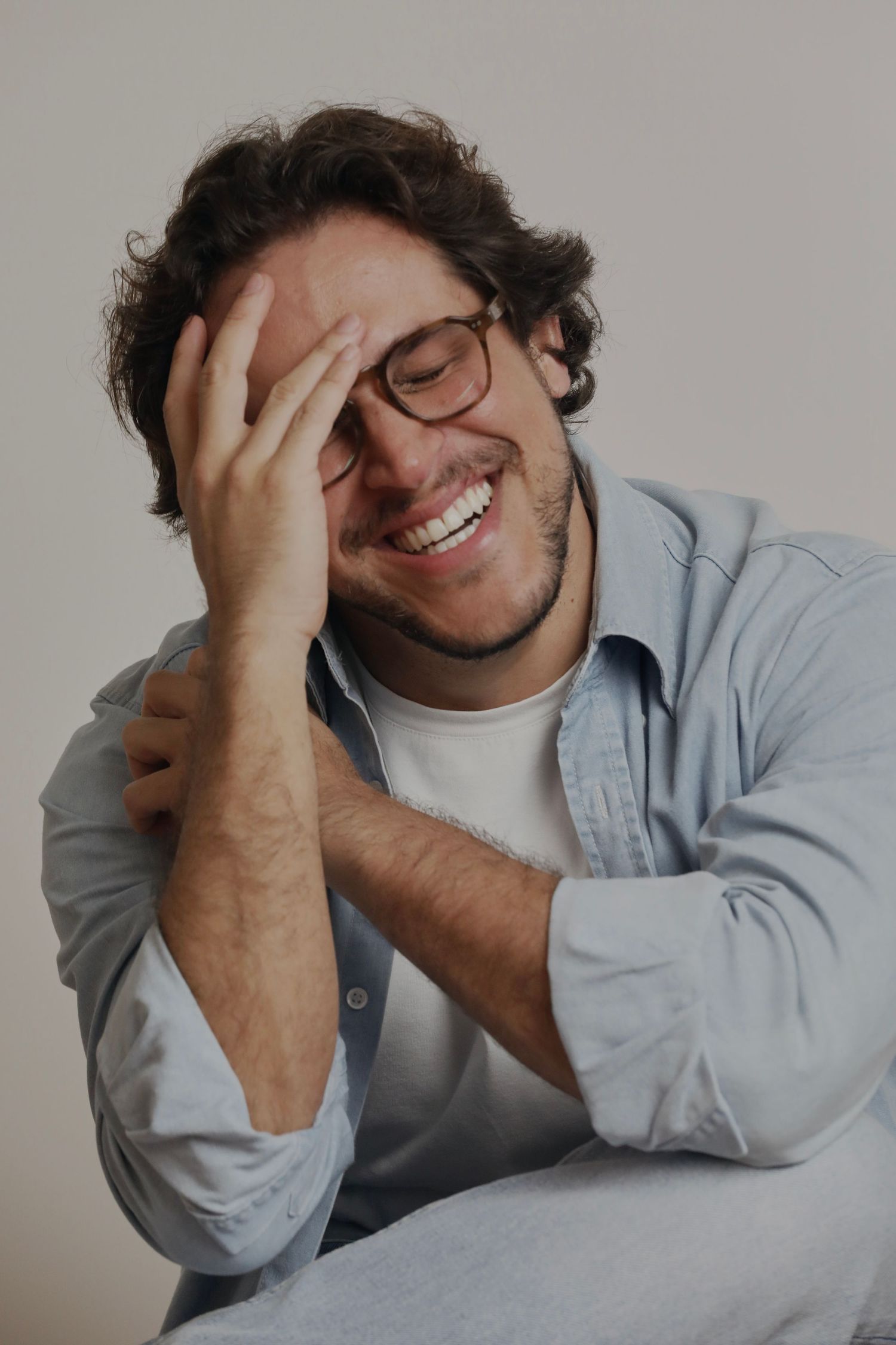 Candid portrait of a person laughing while covering face wearing glasses and casual shirt.
