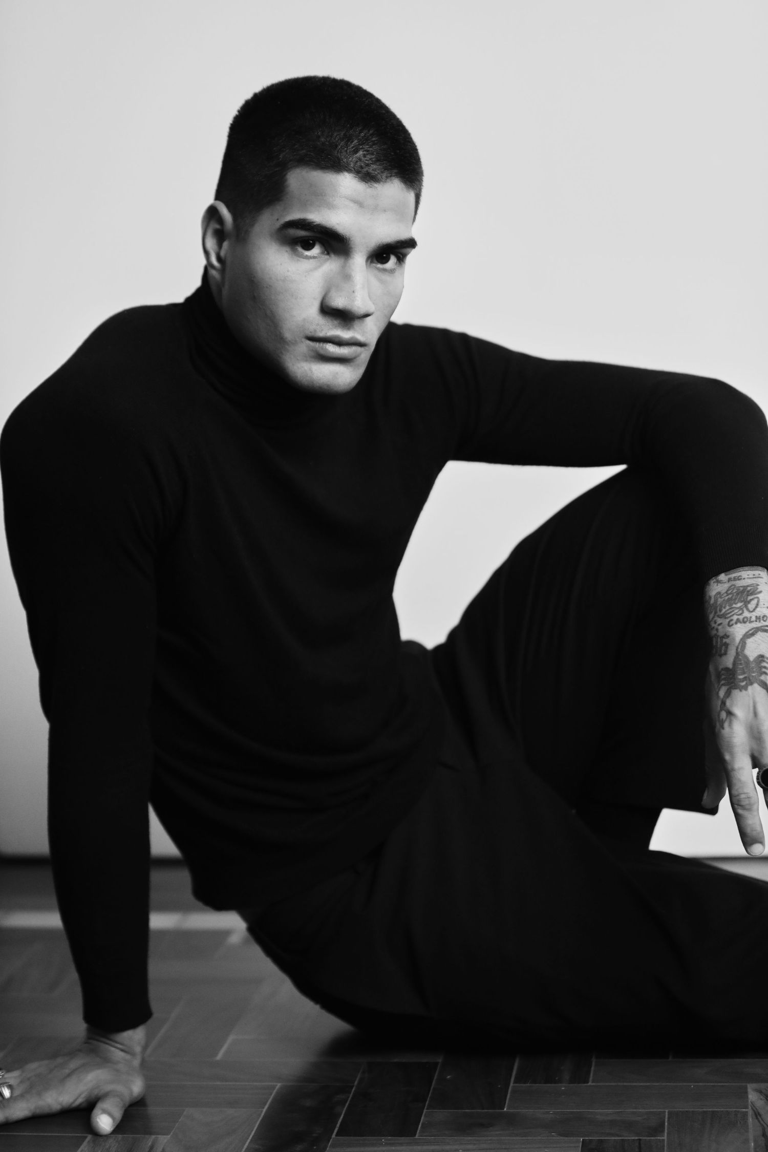 A dramatic black and white portrait of a person in a black turtleneck reclining on a tiled floor.