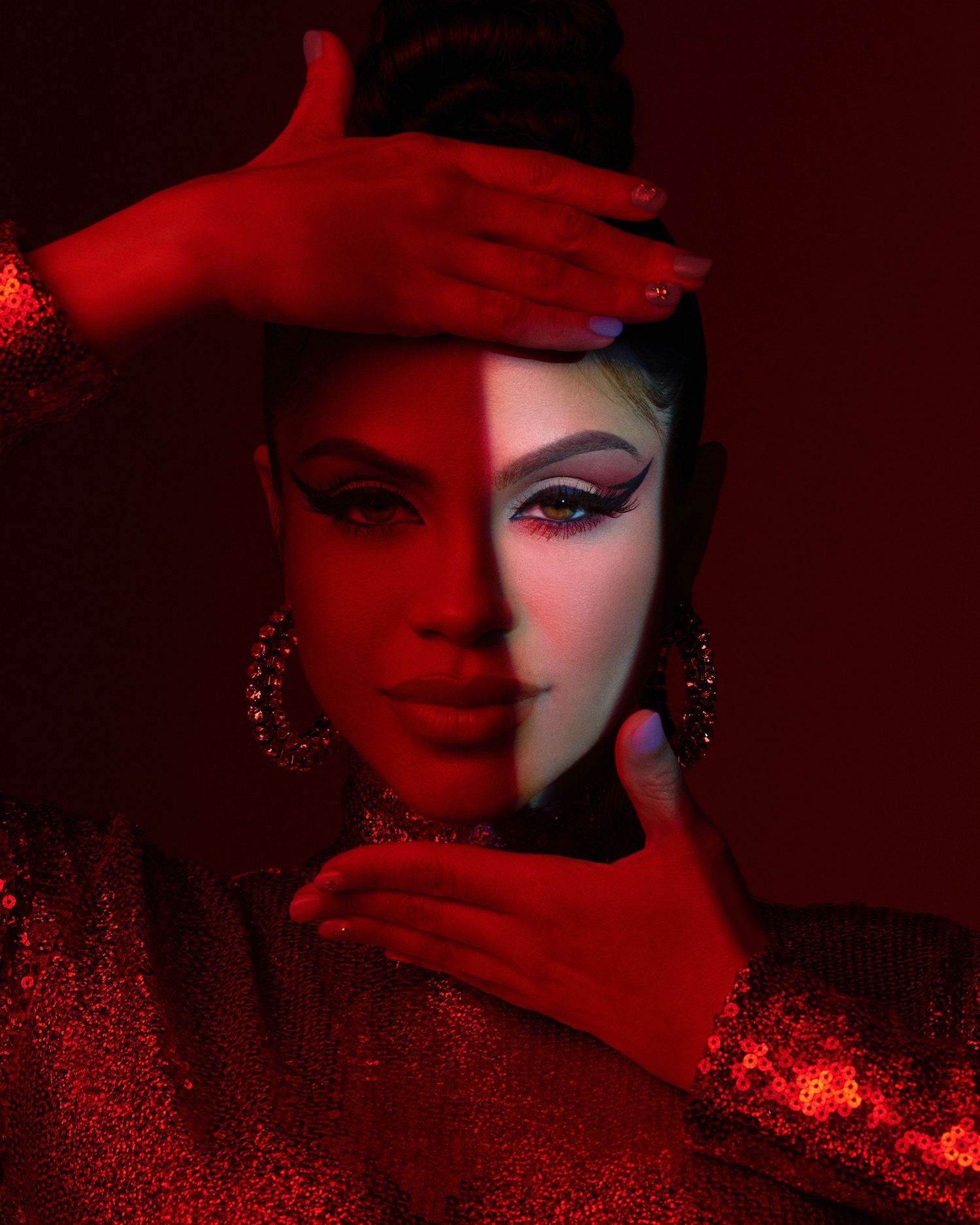 Artistic portrait with dramatic red lighting and glitter-covered hands framing the subject in glamorous makeup and jewelry.