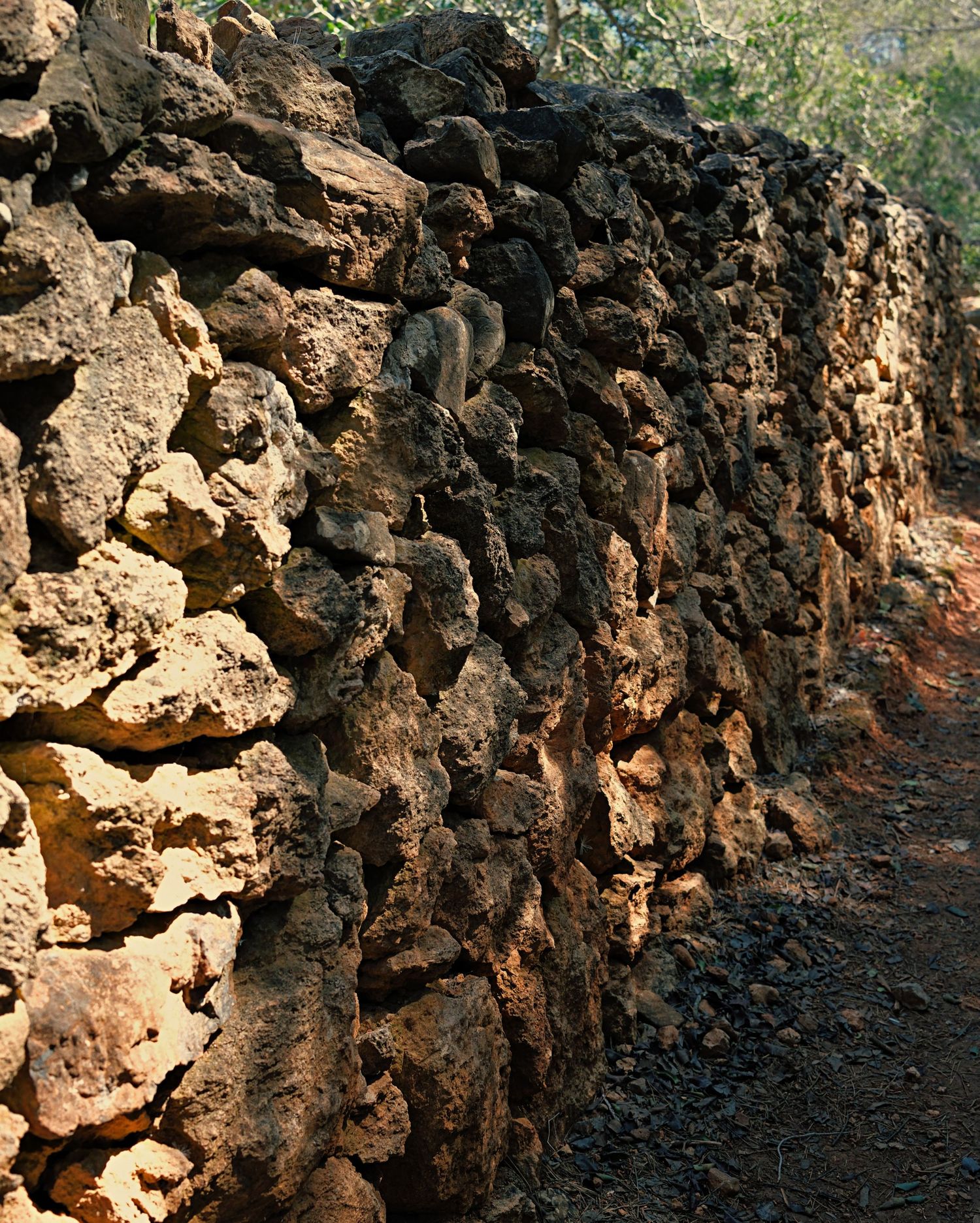 A rugged volcanic rock wall formation shows layers of weathered basalt and soil along a dirt path.