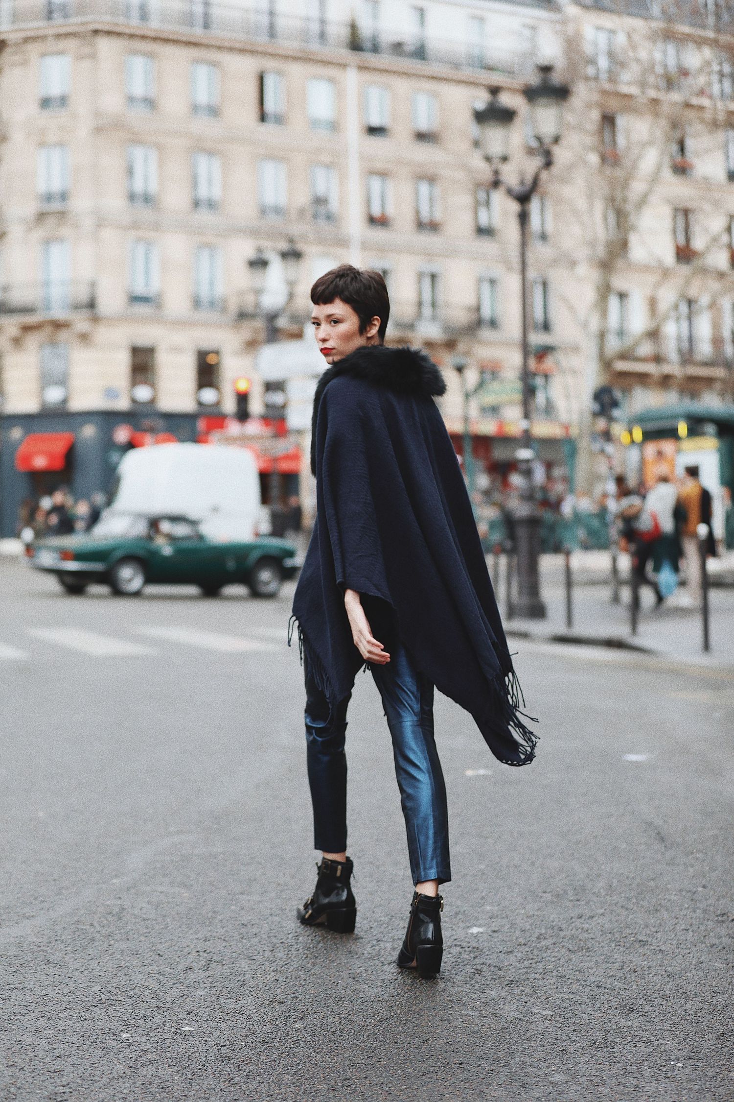 Stylish winter street fashion featuring a black cape coat, cropped jeans and ankle boots on a Paris sidewalk.