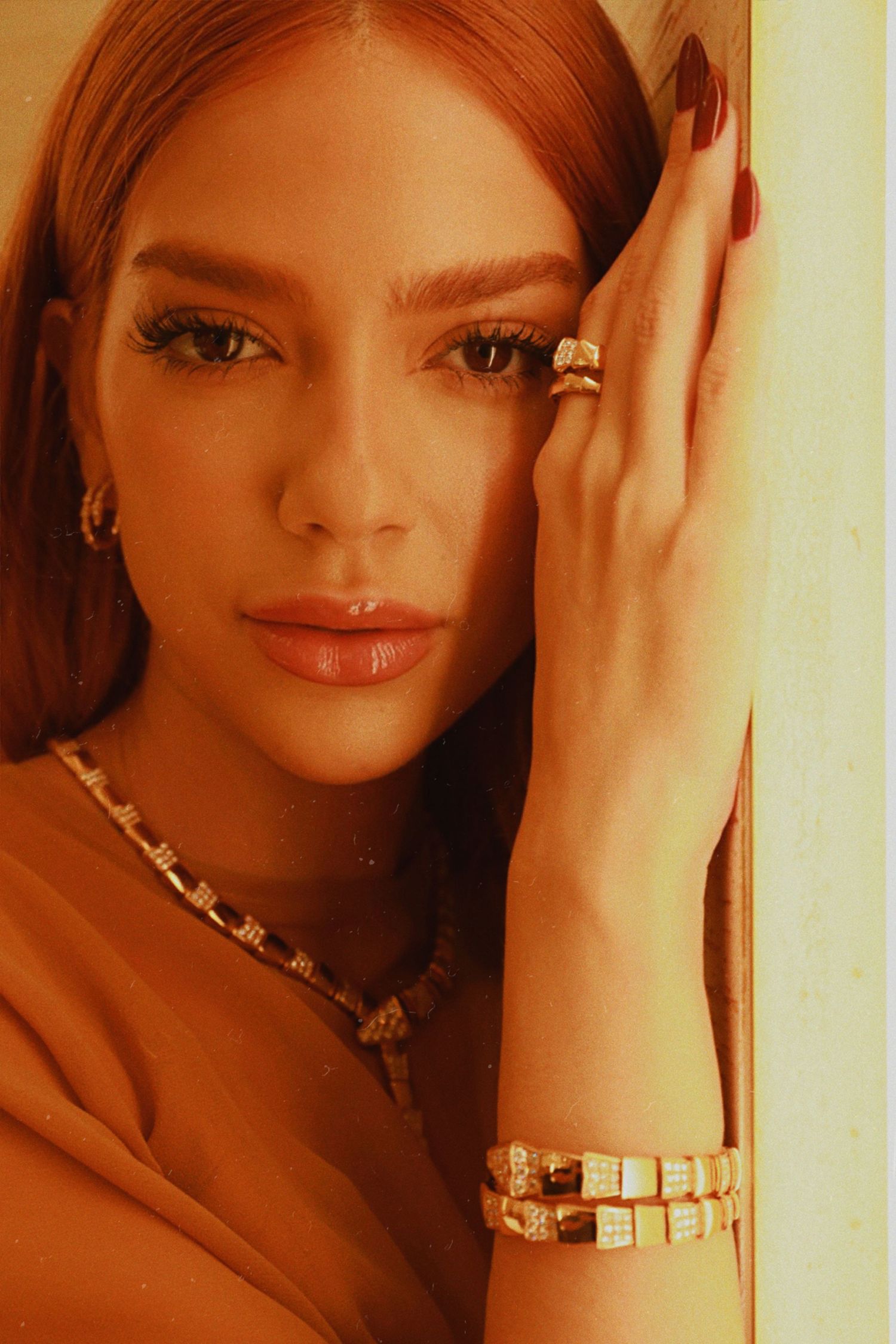 Close-up portrait showing glamorous jewelry and makeup in warm amber lighting.