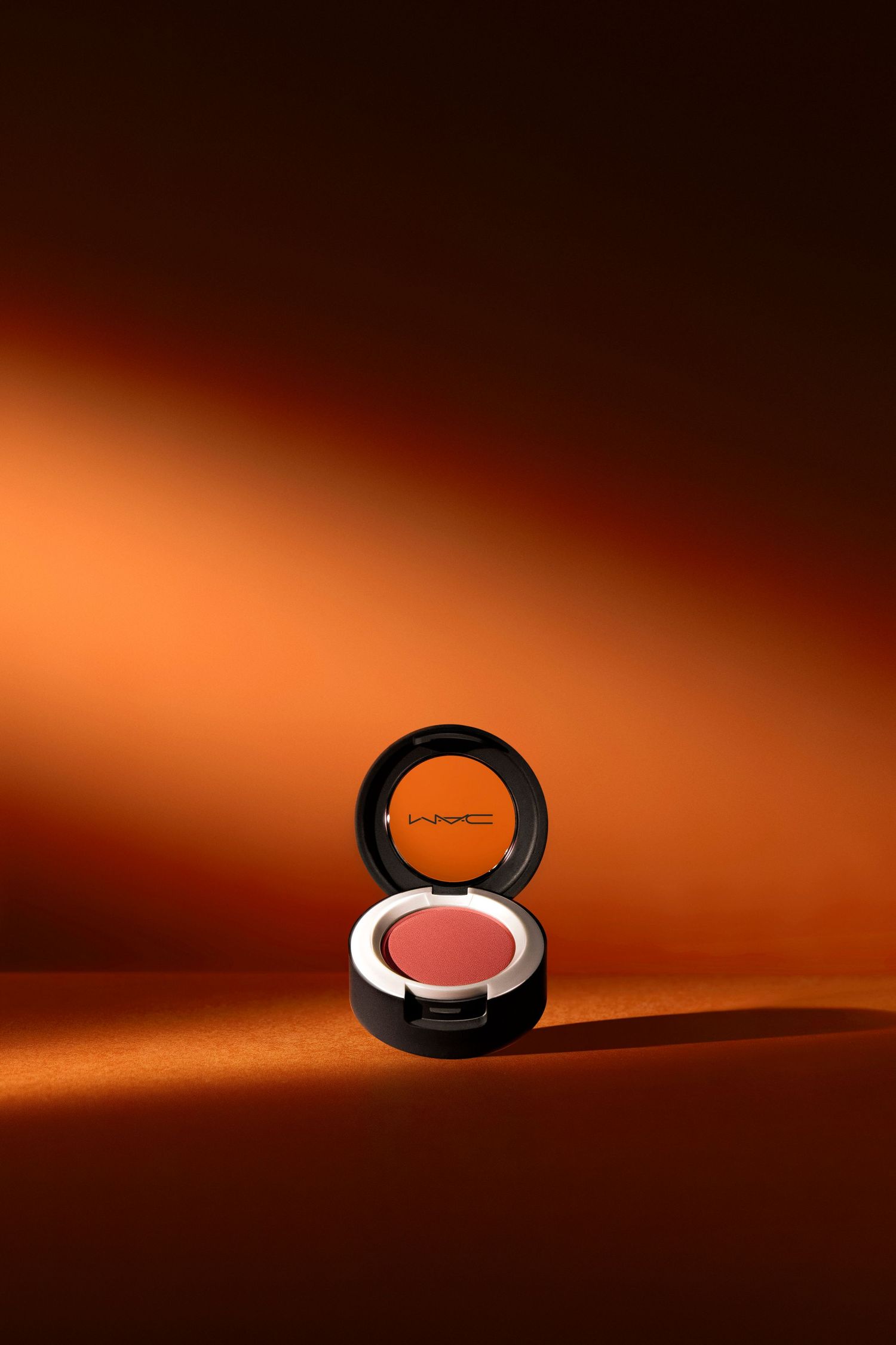 MAC cosmetics powder compact photographed on orange gradient background.
